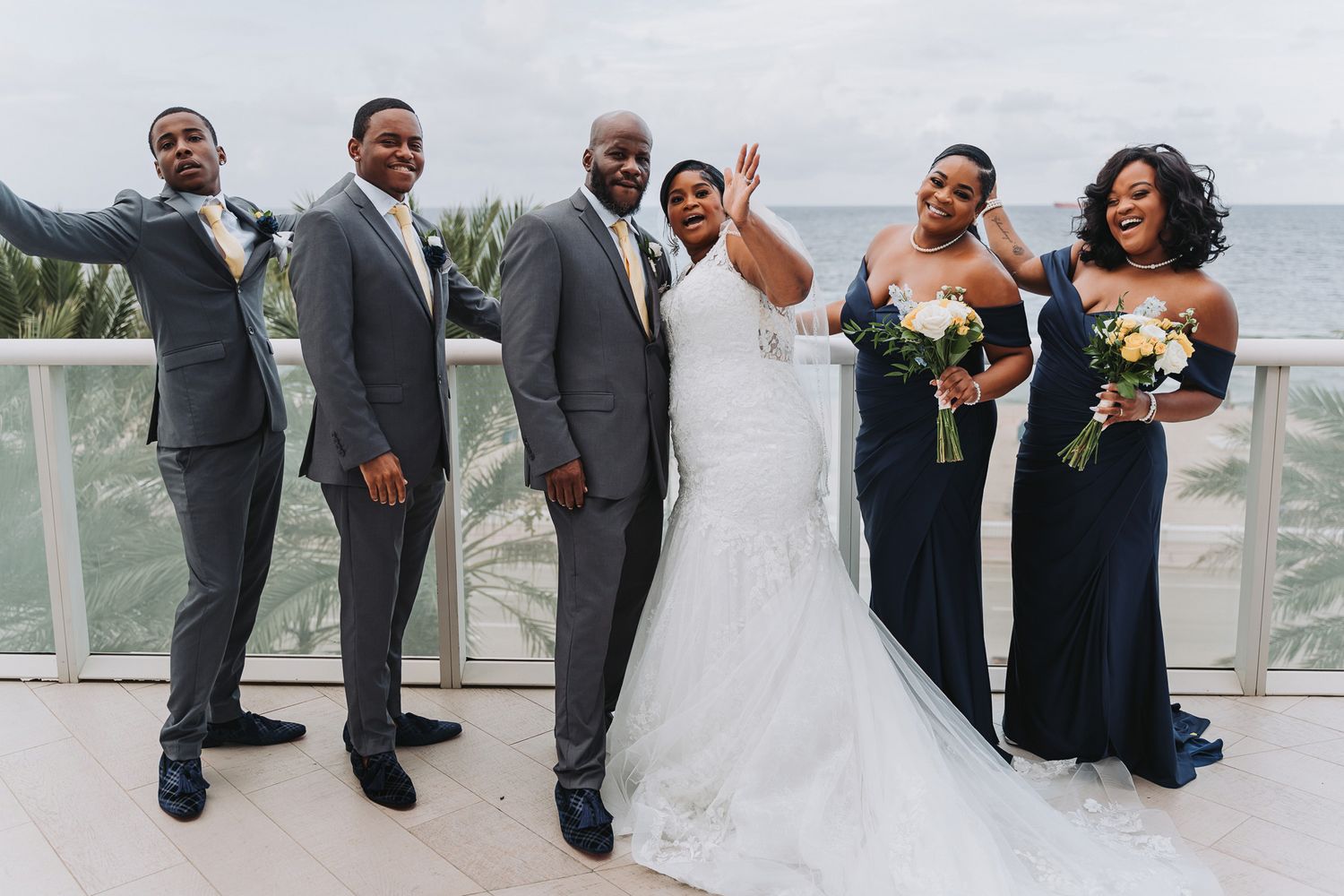 Wedding party poses together on outdoor balcony with ocean view background.