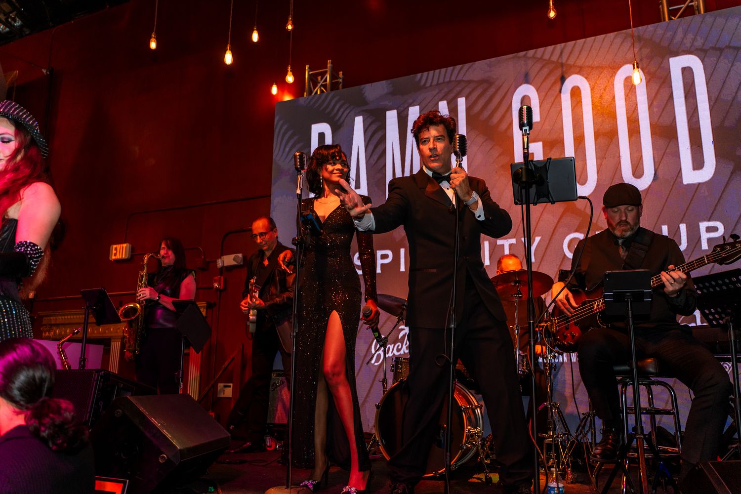 Band performing on stage with red lighting and 'Feel Good' signage in background.