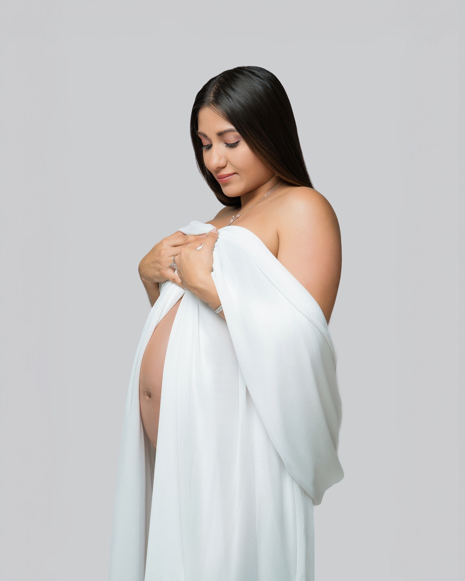 Graceful side view maternity portrait featuring white draped fabric and minimalist styling.