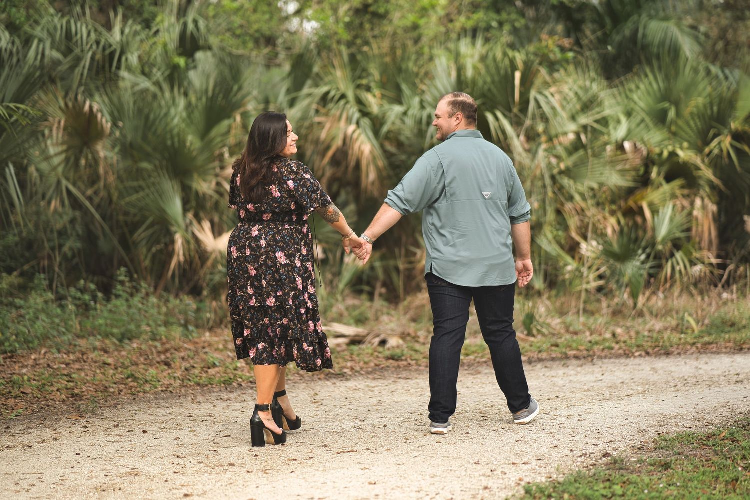 Couple walking hand in hand on a nature trail with palm trees.