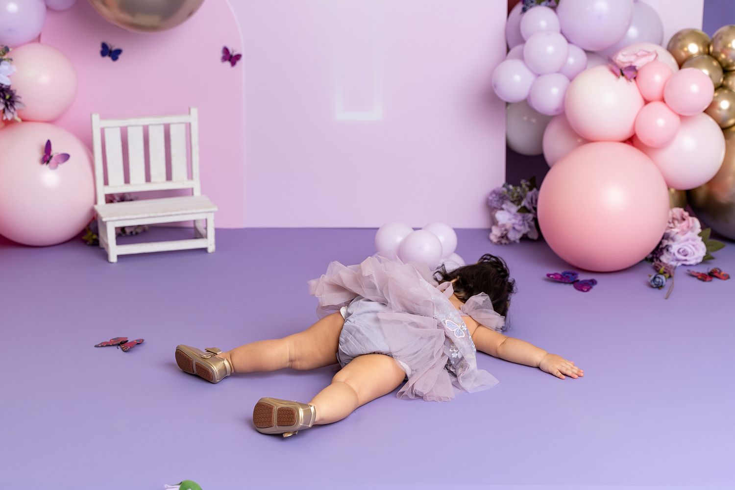 Pink and purple birthday photo setup with a small chair and scattered butterfly decorations.