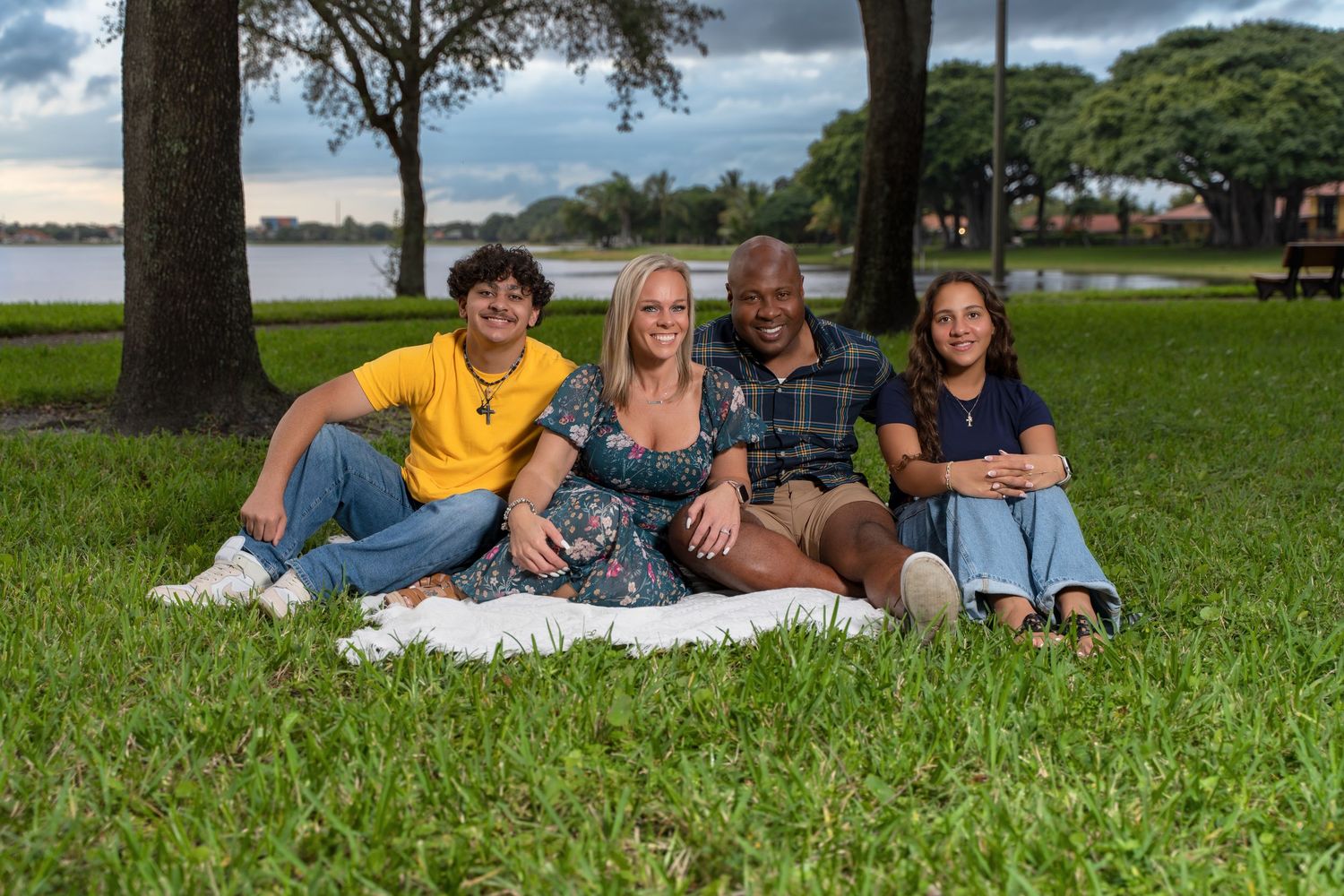 Group of people lying on green grass outdoors on a sunny day with trees in the background.