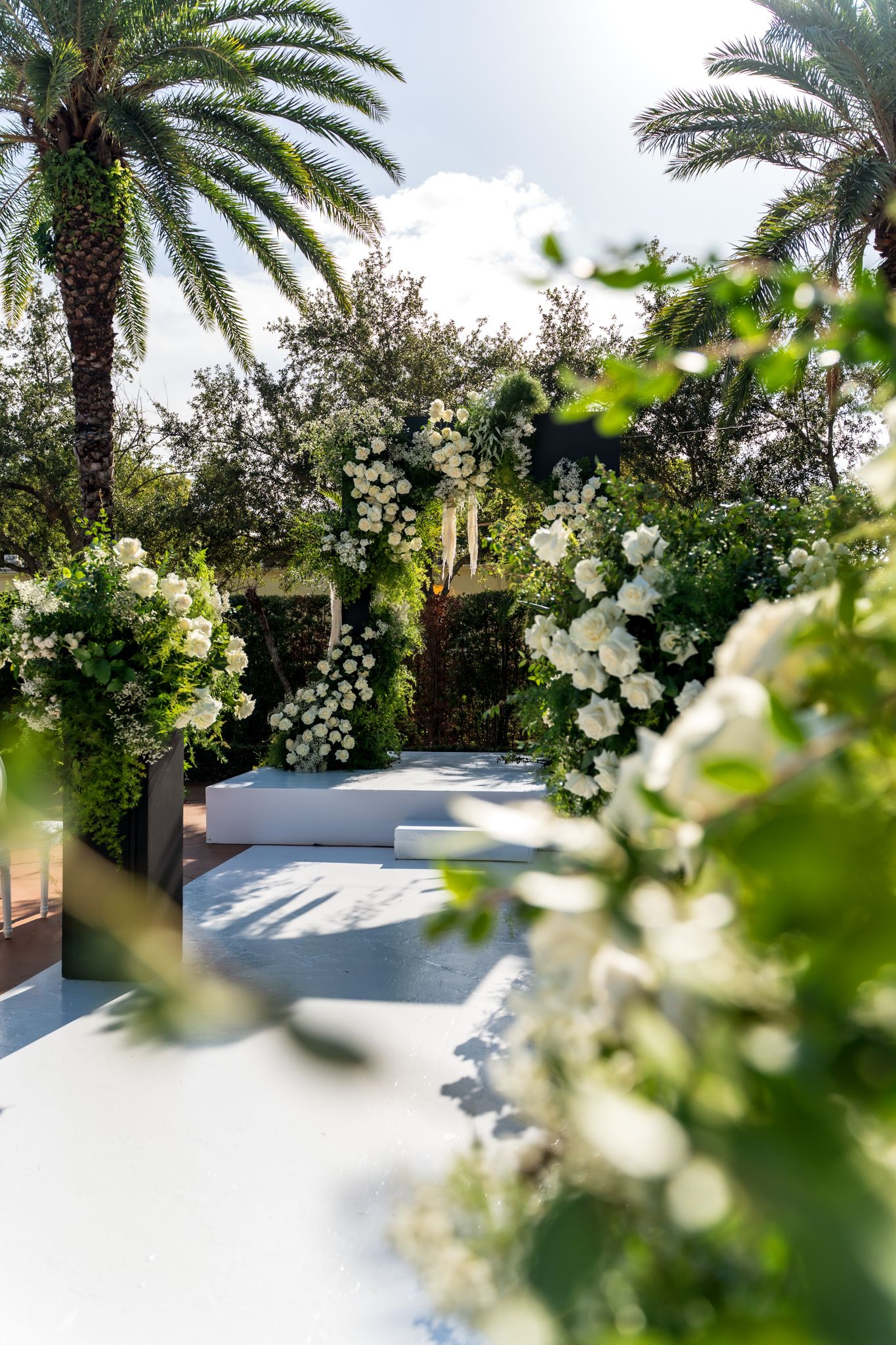 Lush wedding venue with white floral decorations and palm trees creating a tropical paradise setting.