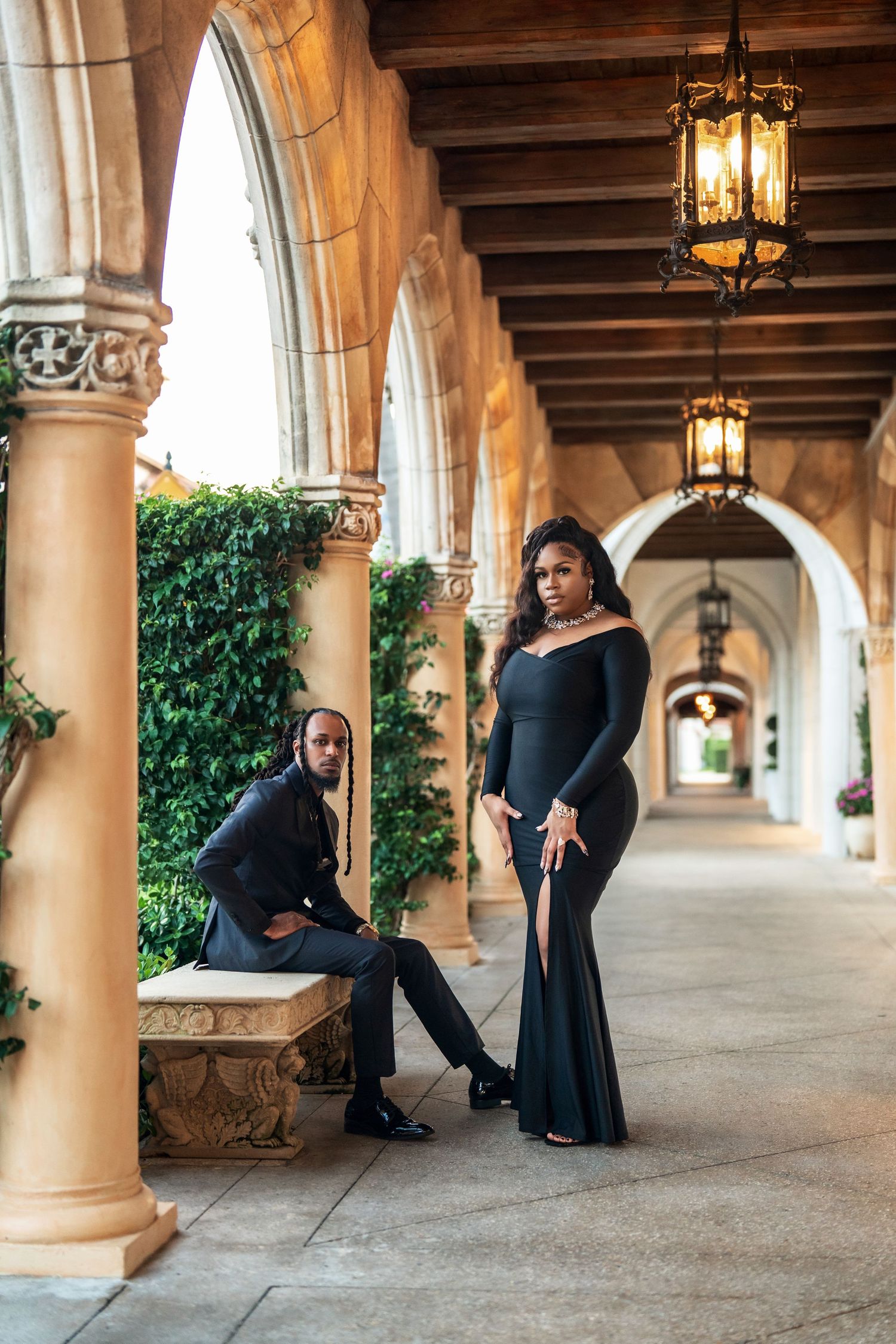 A couple poses romantically under elegant archways with stone columns and hanging lanterns during an engagement photoshoot.
