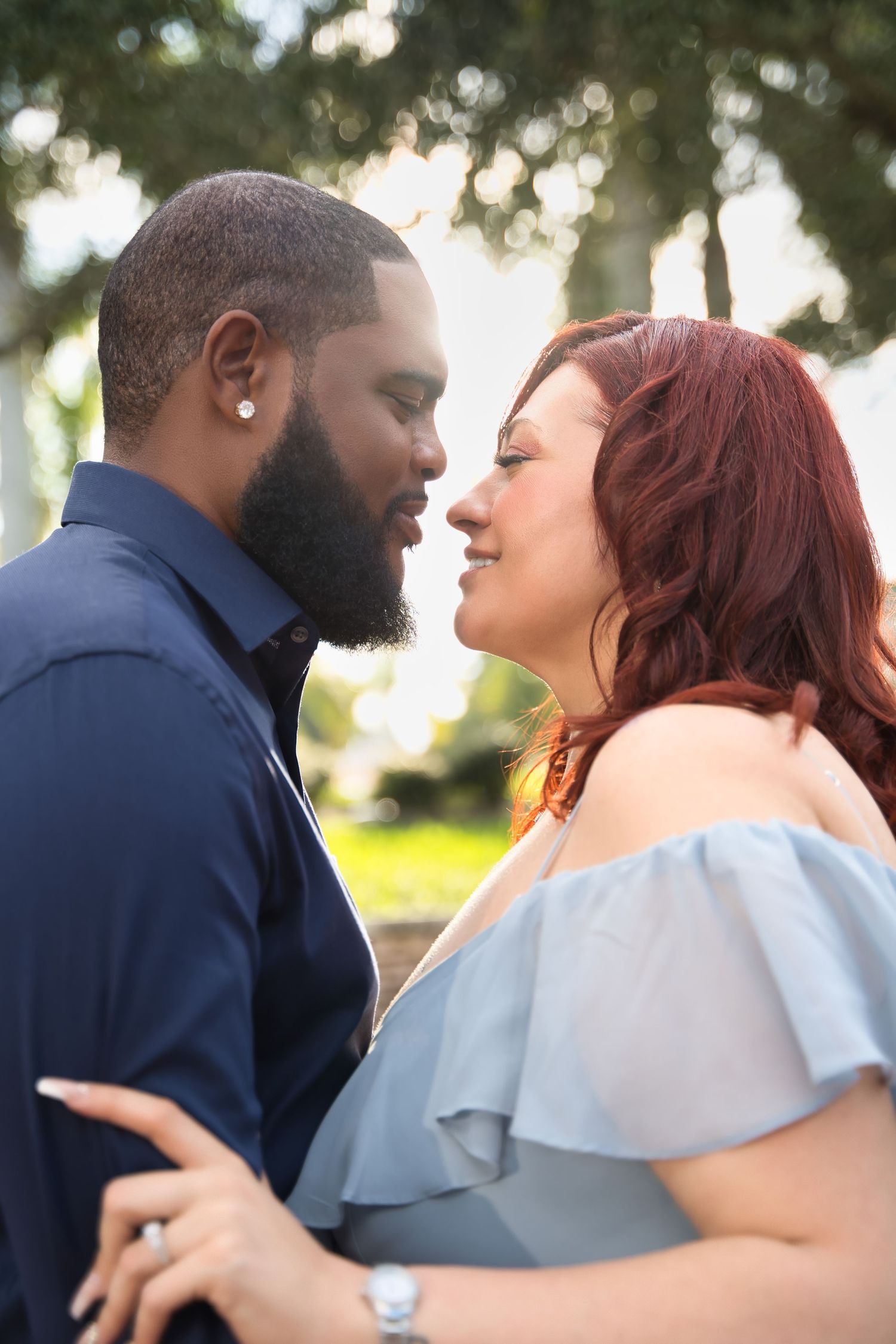 A romantic couple in blue attire embrace while sharing a tender moment in a garden setting.