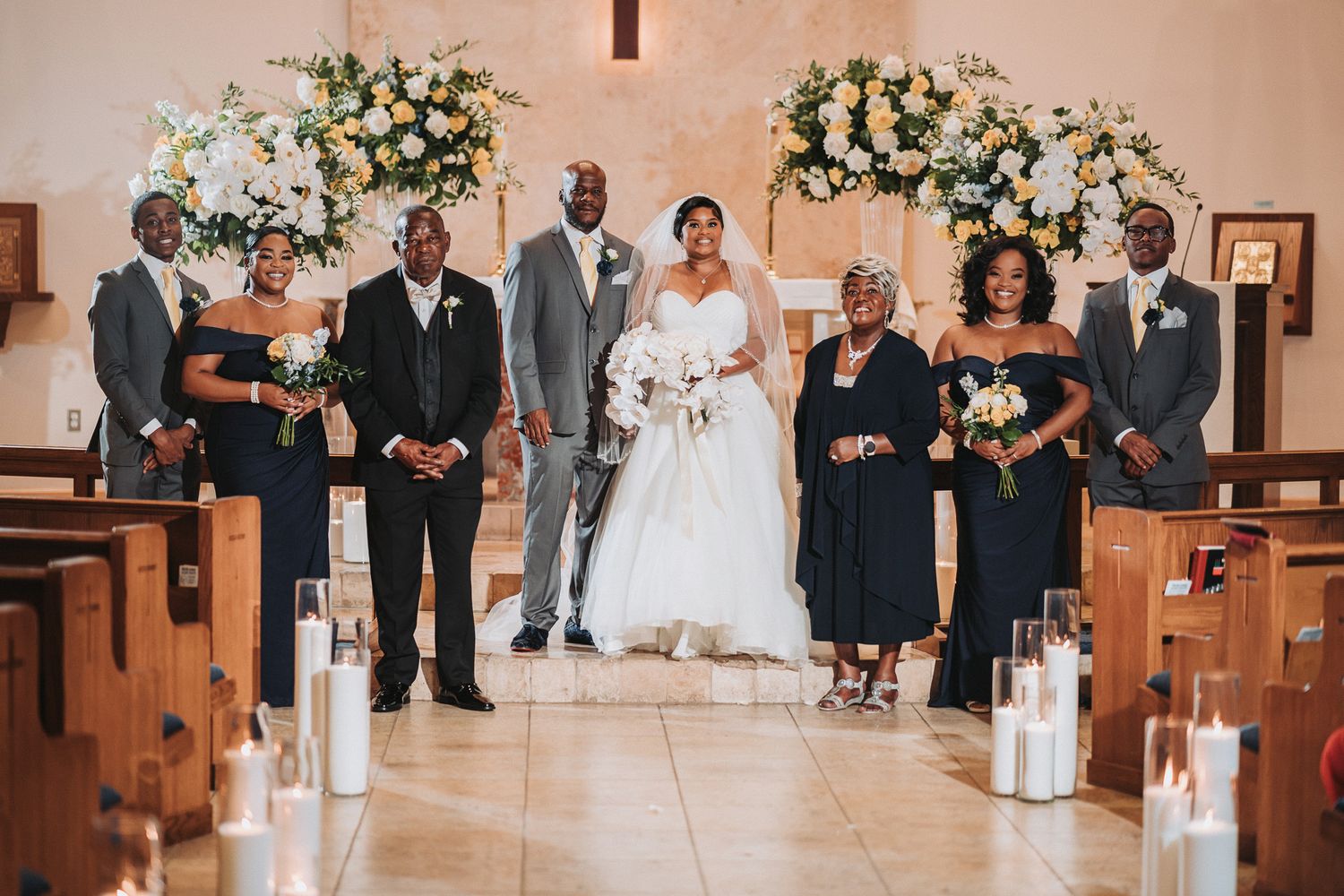 Wedding party poses formally in church with bride in white gown and attendants in navy blue.