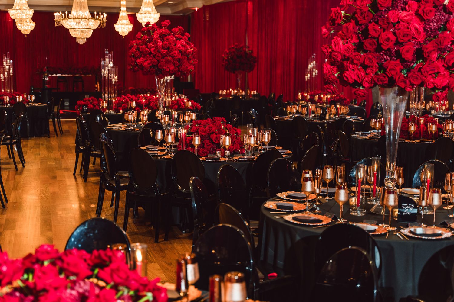 Elegant reception hall decorated with red roses, black linens, and crystal chandeliers.