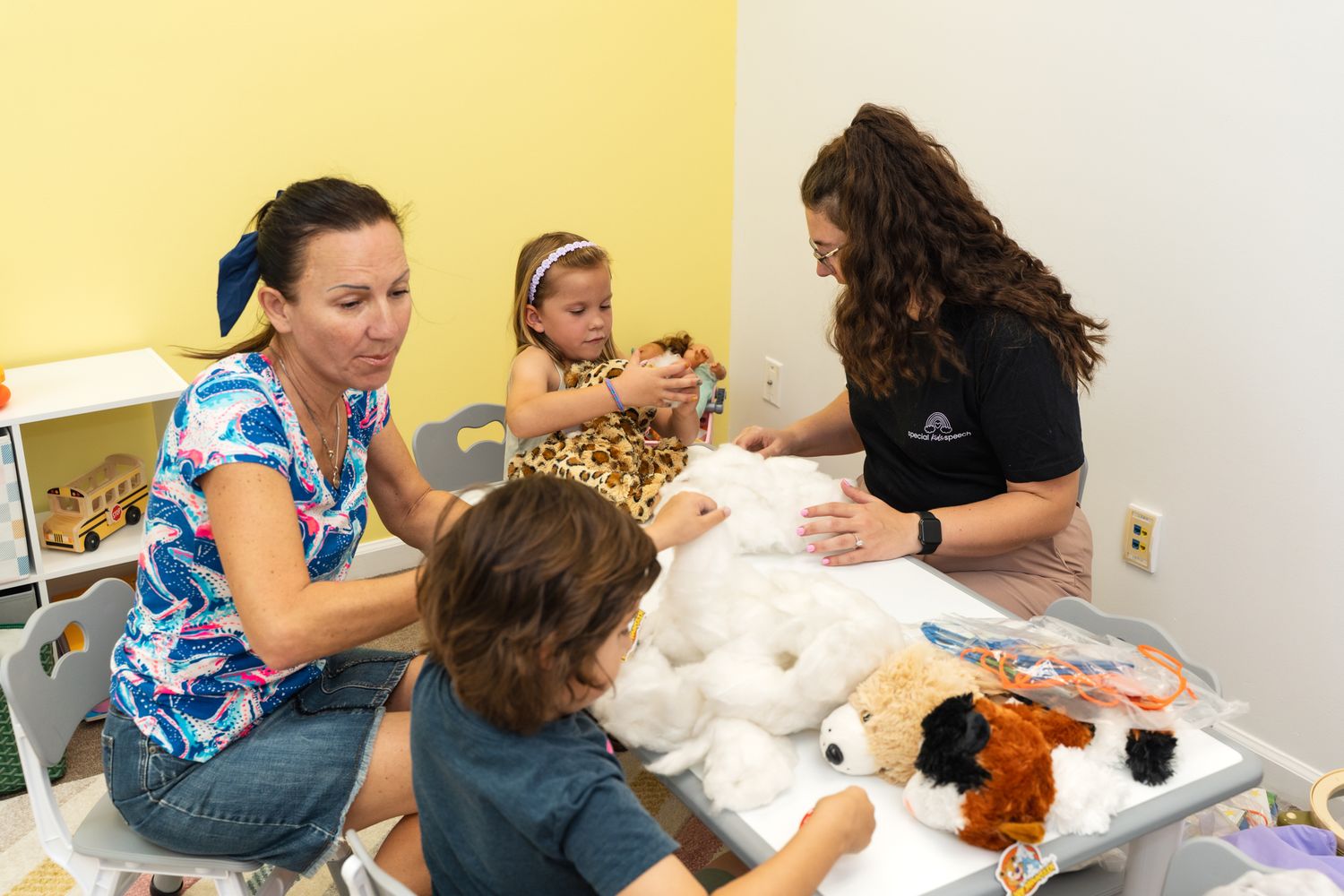 Children and adults participate in a hands-on creative activity with stuffed animals and craft supplies in a bright room.