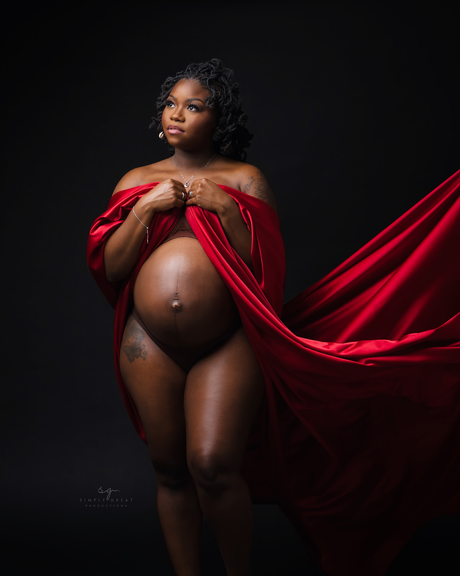Artistic maternity portrait featuring flowing red fabric against dark background.