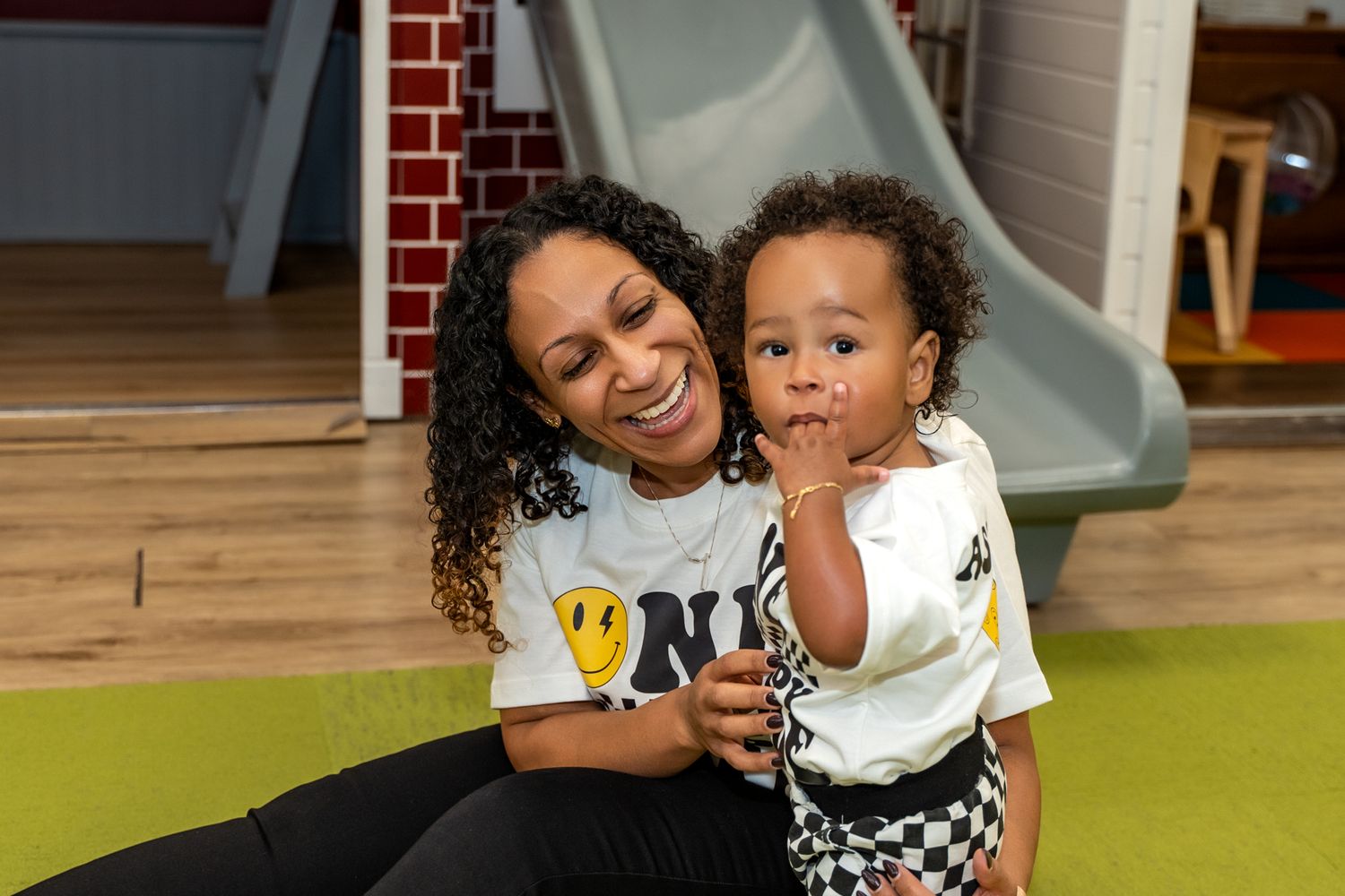 A joyful moment shared between caregiver and toddler on green carpet.