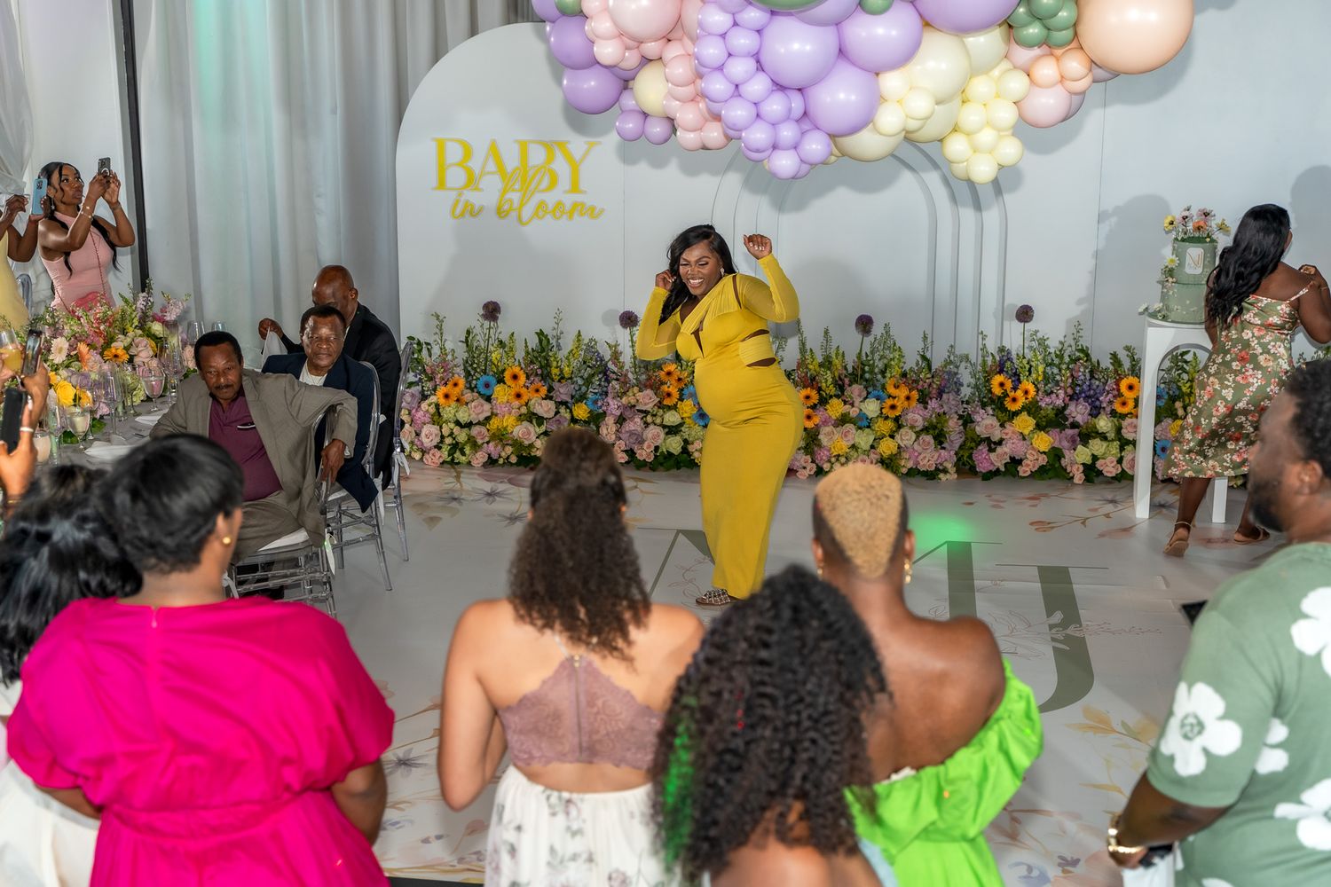 Celebration in a bright room decorated with pink and purple balloon garlands and floral accents.