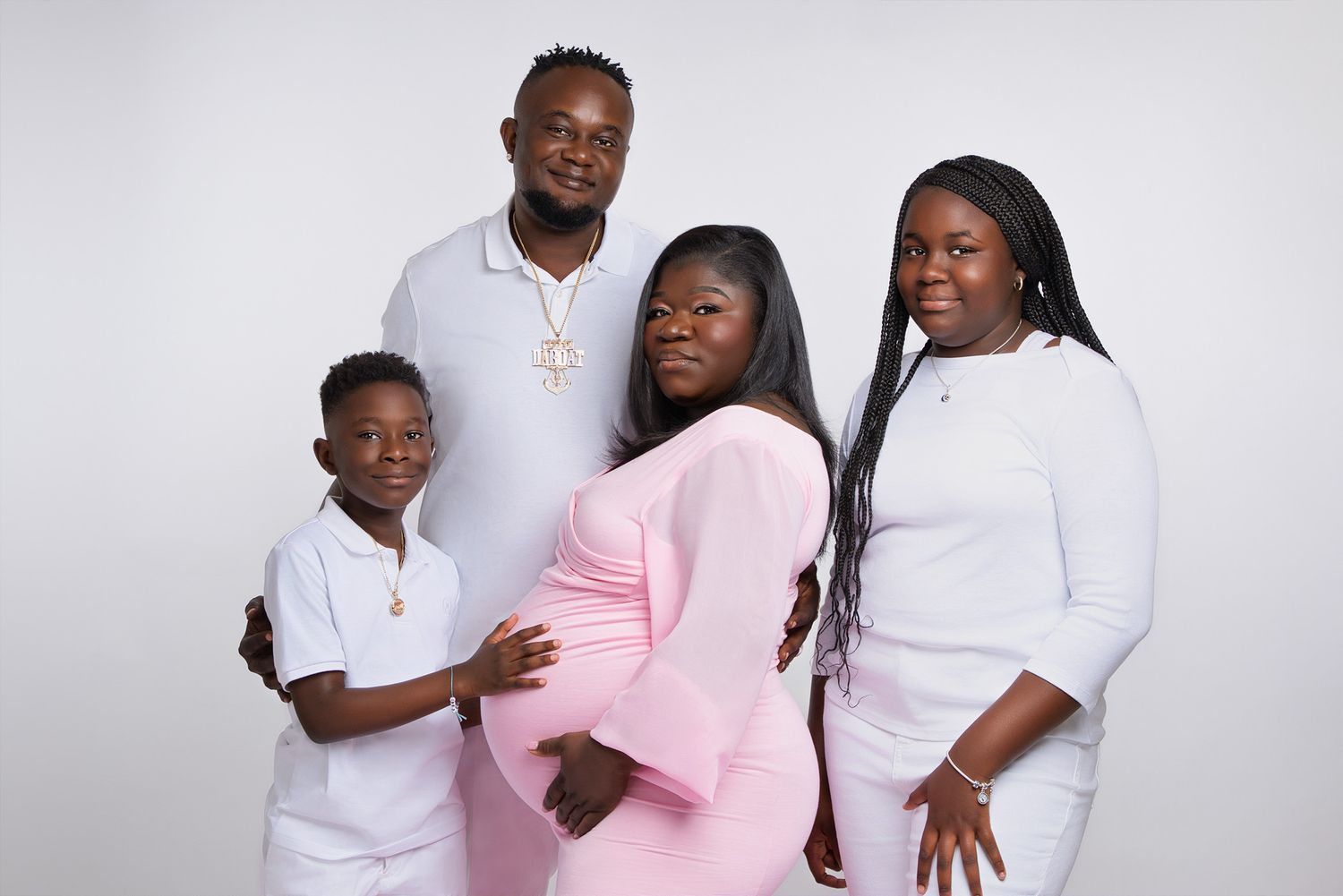 Happy family portrait with matching white outfits around expectant mother in pink dress.