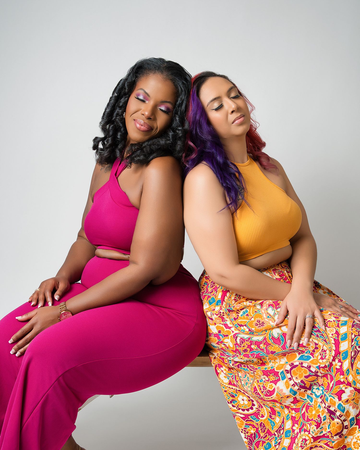 Models in pink and yellow outfits pose back-to-back during fashion photoshoot.