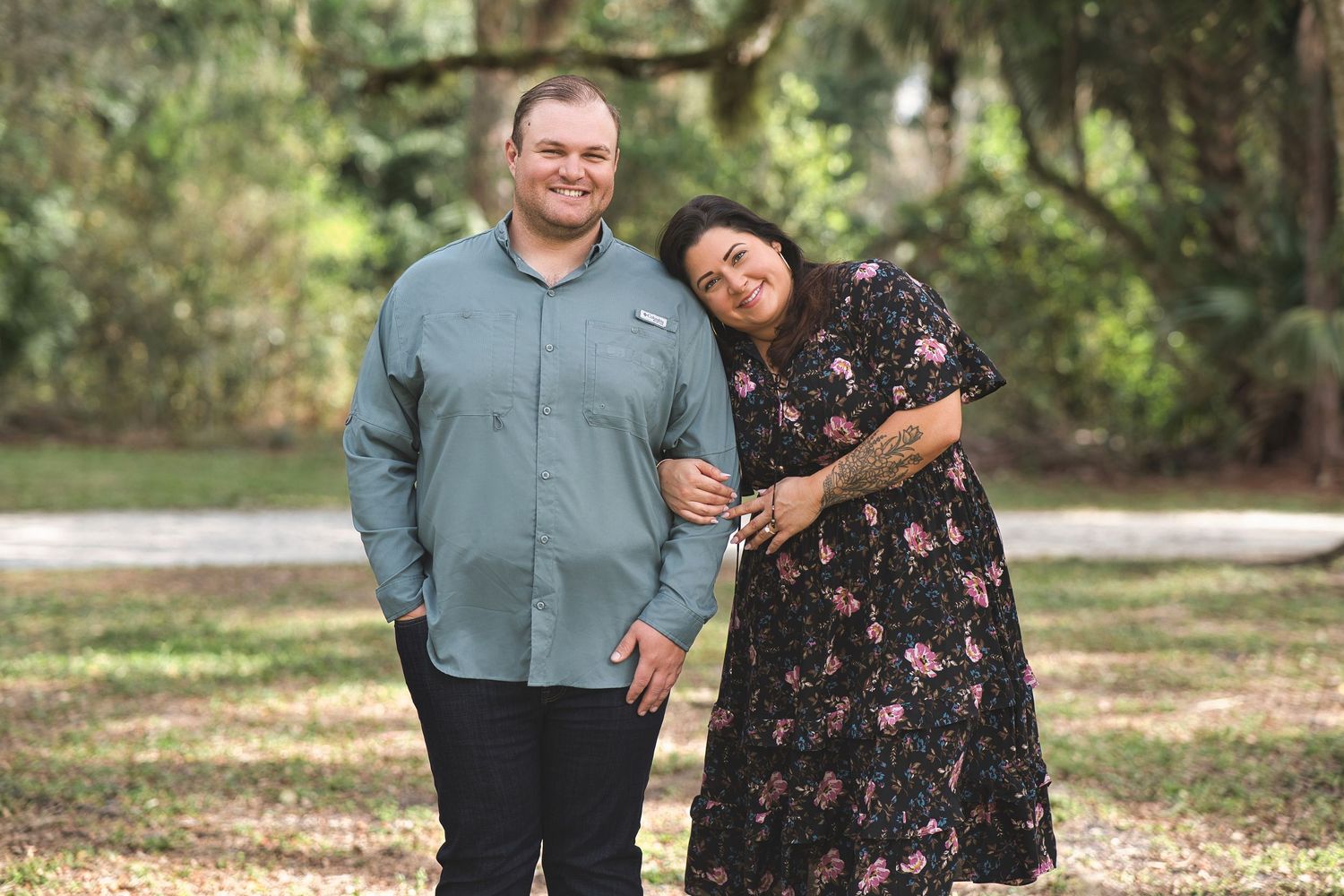 Happy couple posing playfully together in a park with trees in the background.