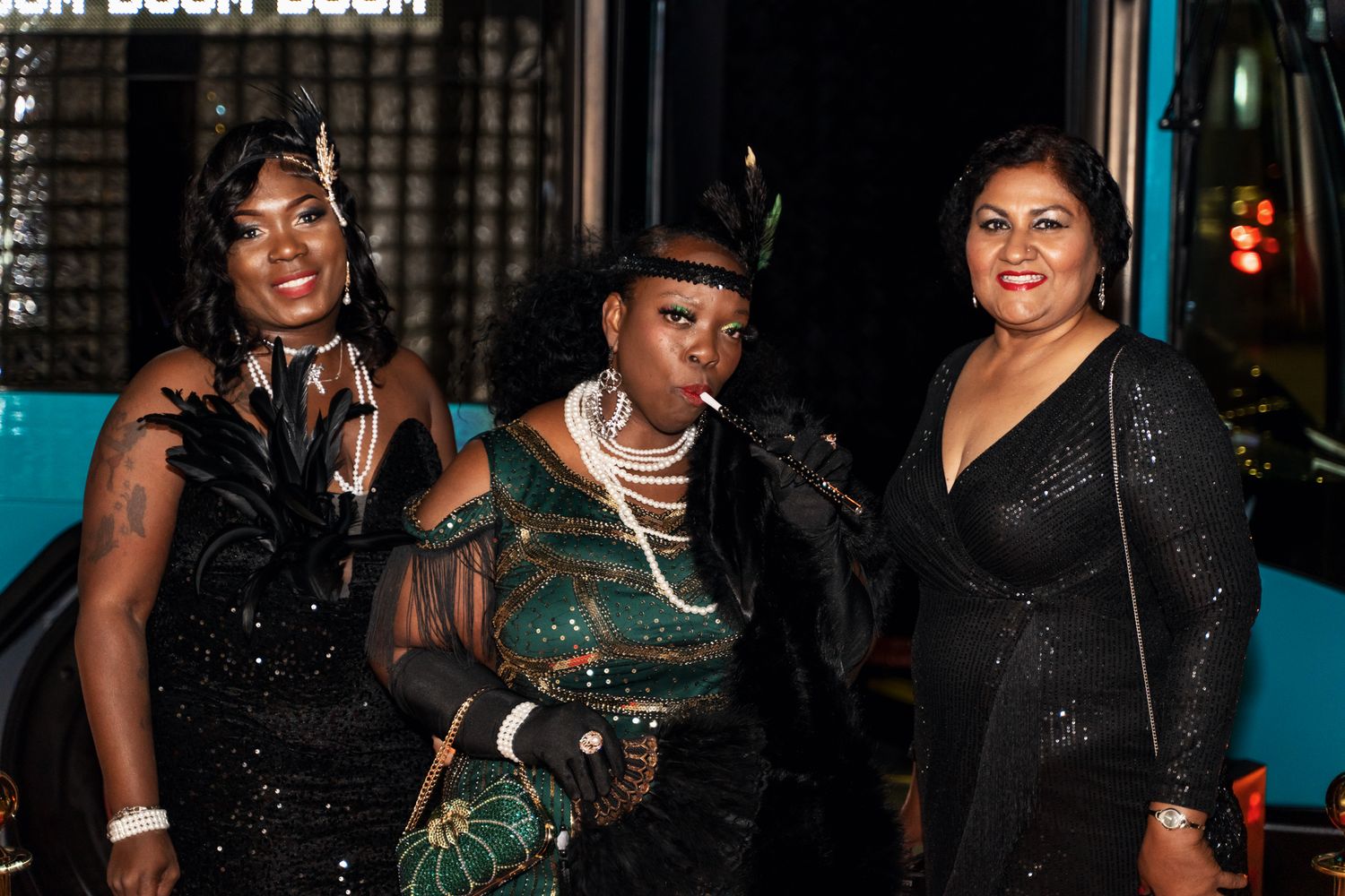 Three guests in glamorous black and green evening attire pose together at a formal event.