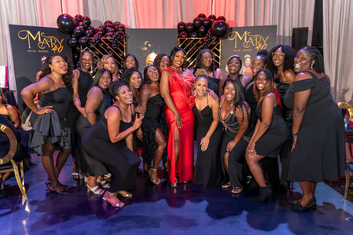 Large group photo of party guests in black dresses posing with someone in a standout red gown.