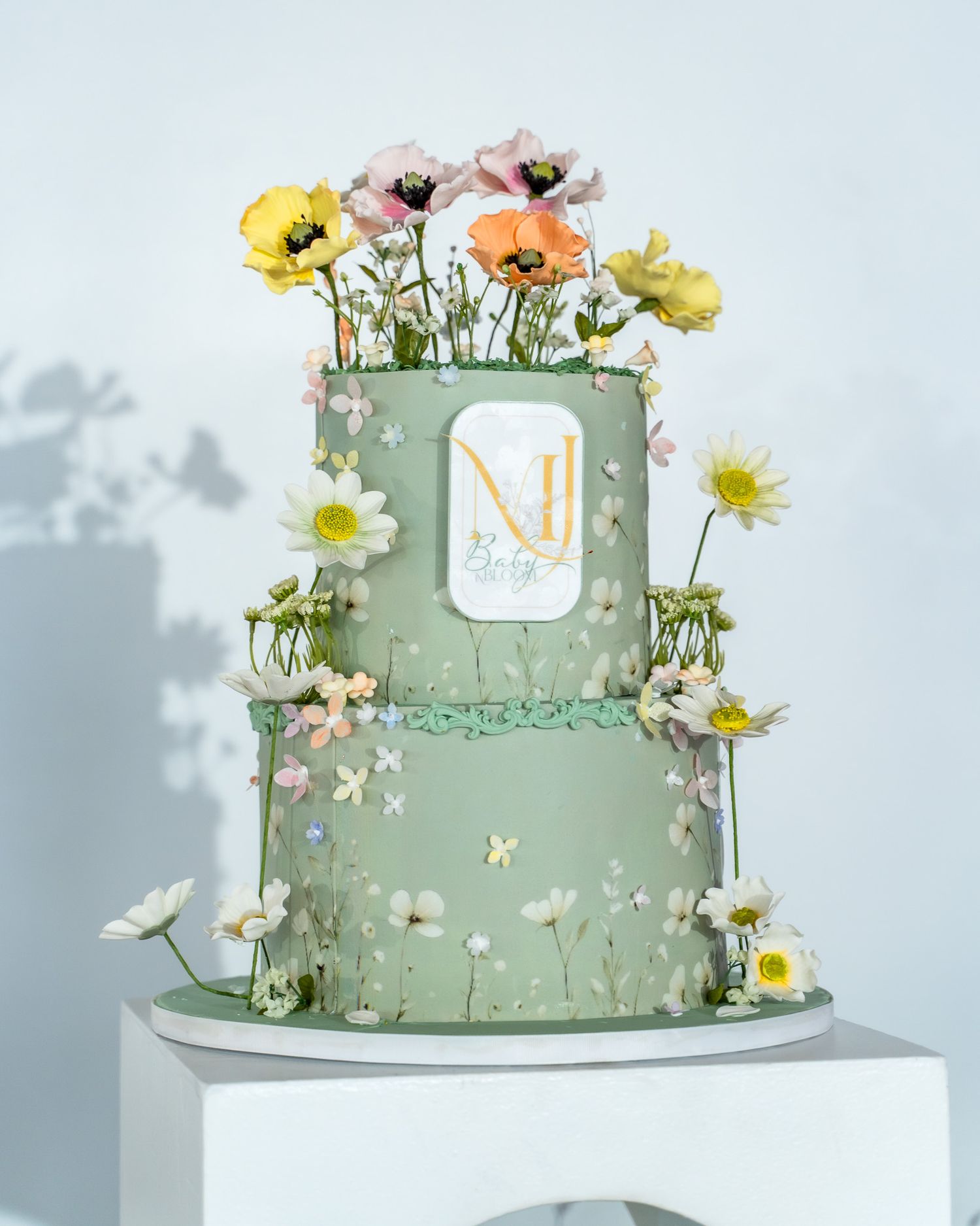 Two-tier mint green cake decorated with fresh flowers and delicate botanical details.