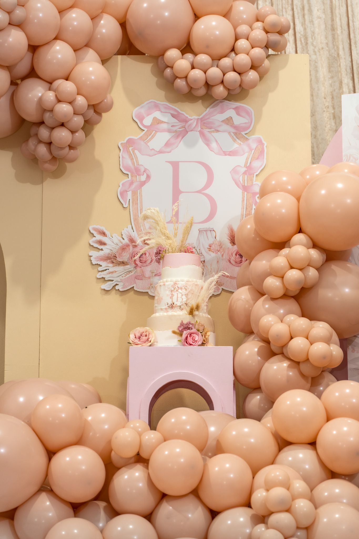 Pink monogram display with balloon garland and cake pedestal for baby celebration.