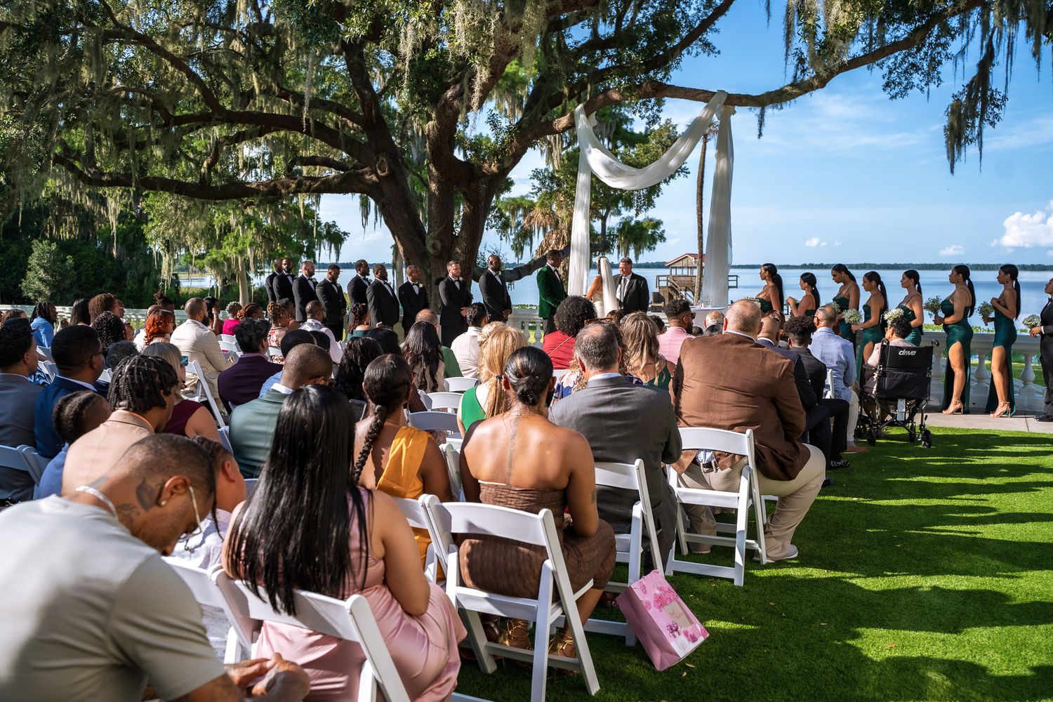 Wedding guests seated outdoors under a large oak tree draped with Spanish moss.