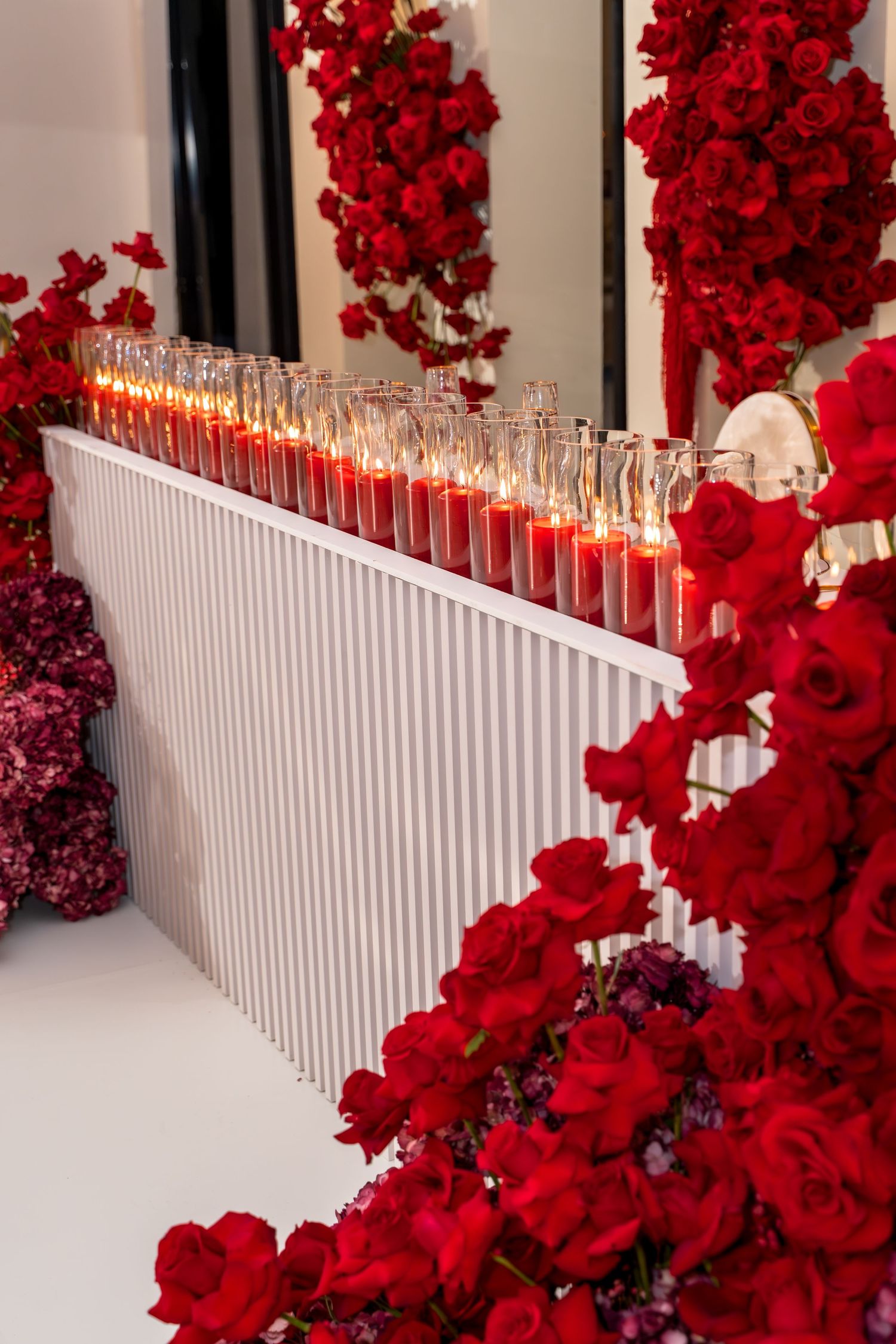A white picket fence decorated with vibrant red roses and glowing candles creates a romantic ambiance.