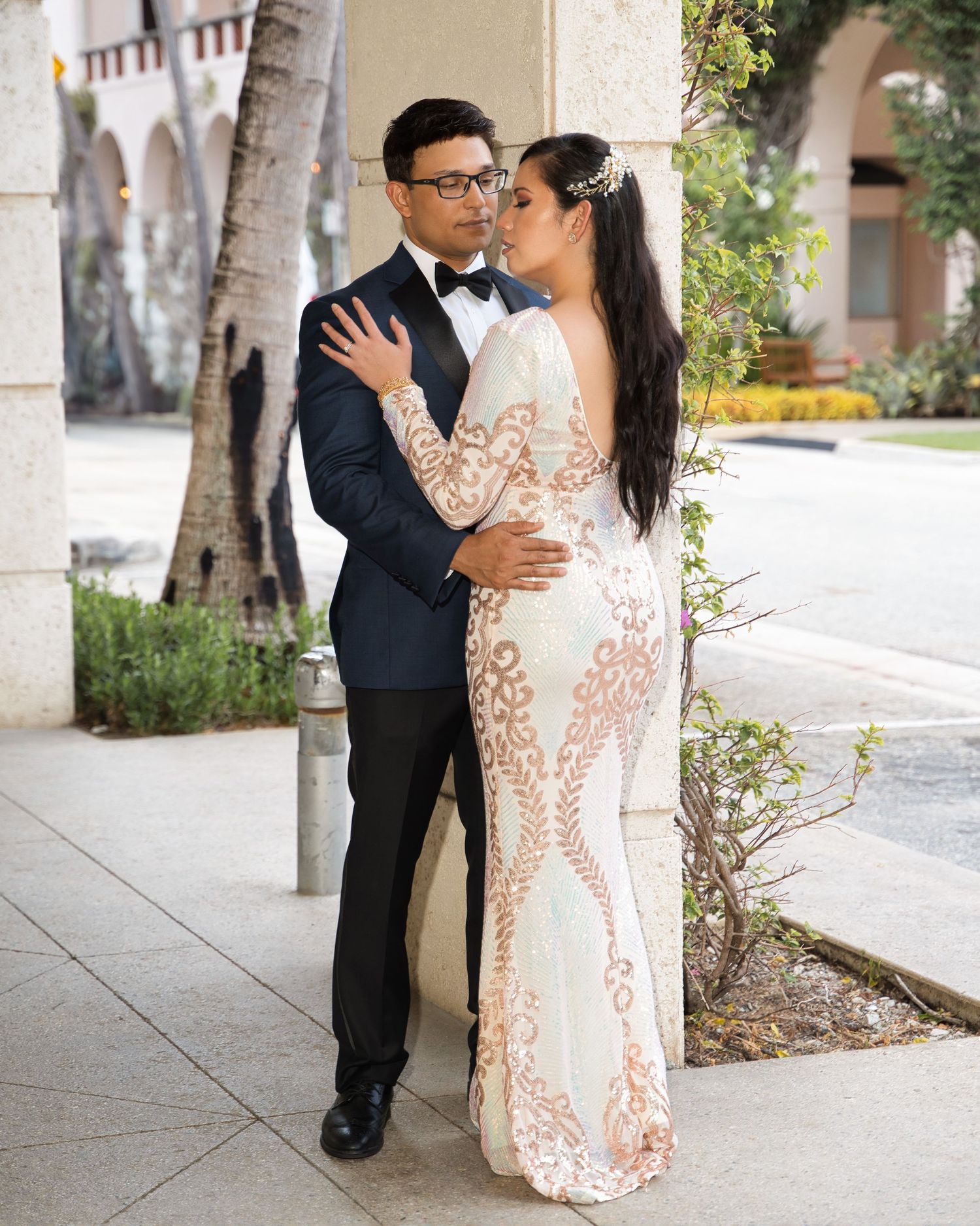 Newlywed couple in elegant wedding attire posing against architectural columns.