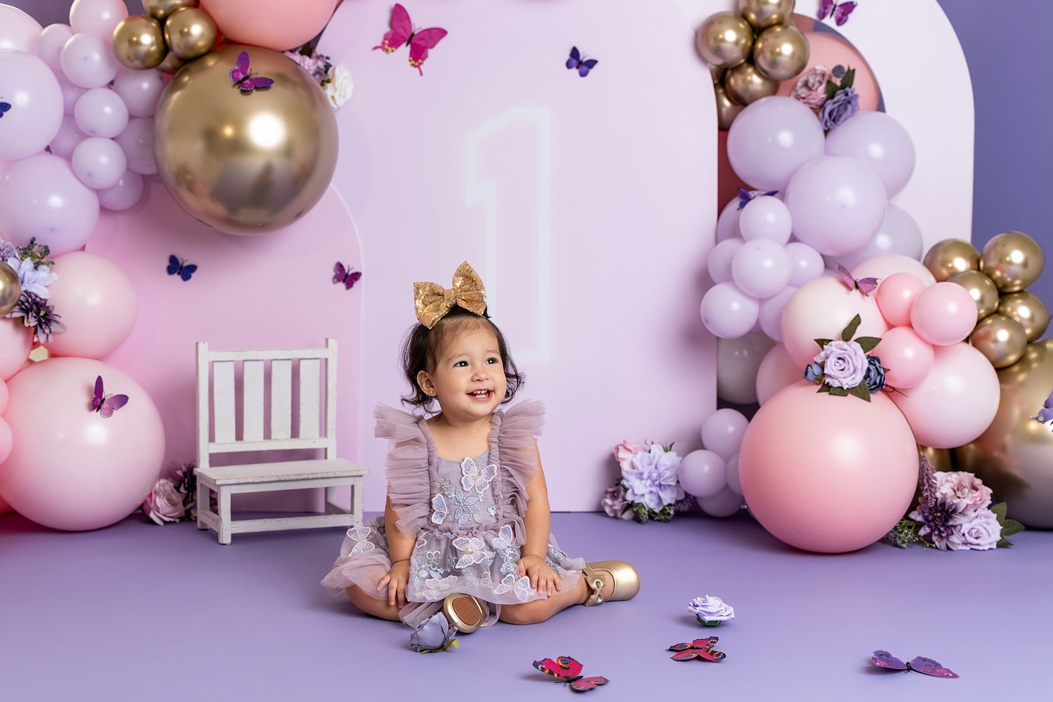 Dreamy pink and purple balloon backdrop with white chair and butterfly decorations for baby photography.