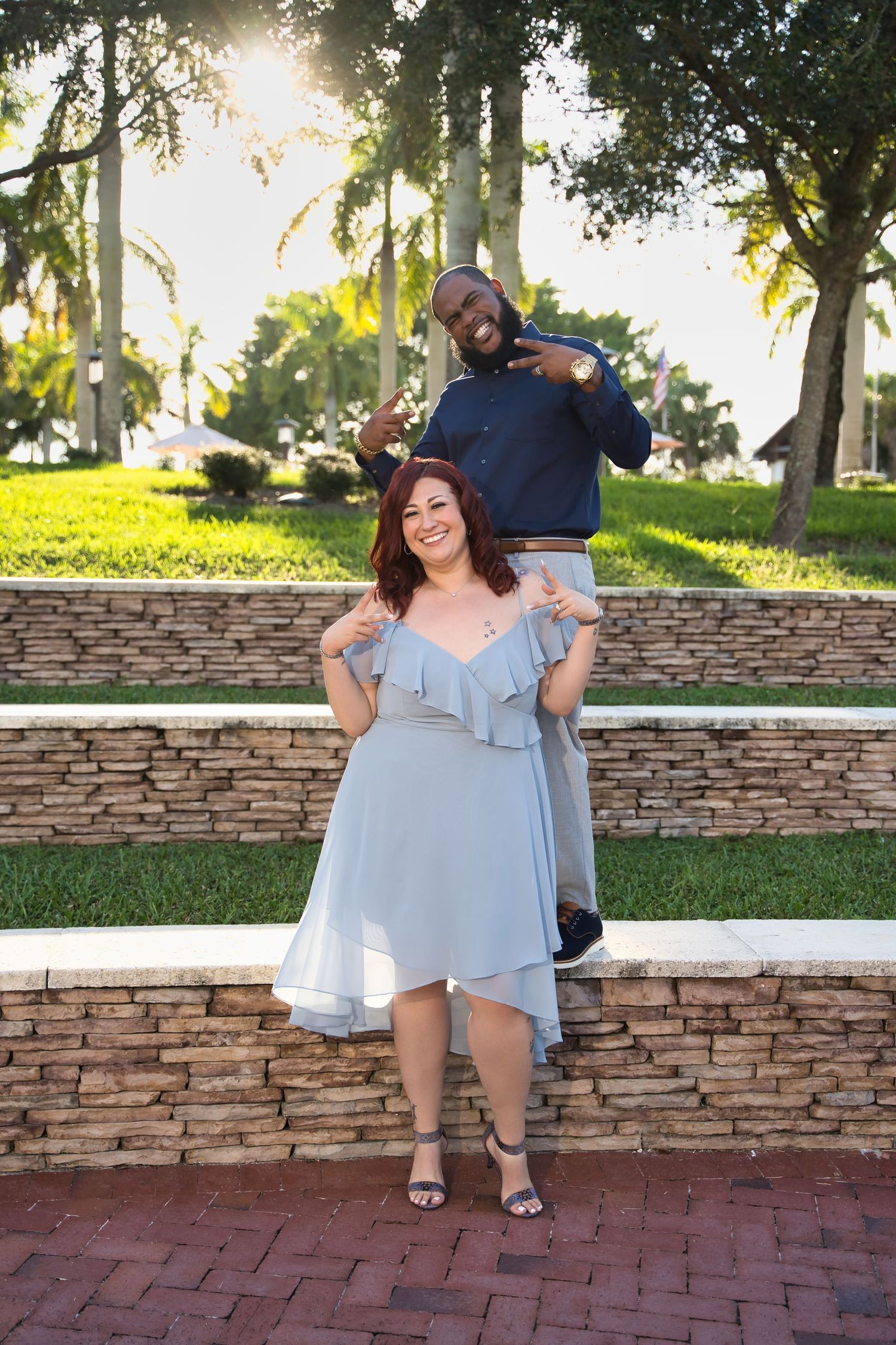 A playful couple poses on stone steps with tropical palm trees in the background.