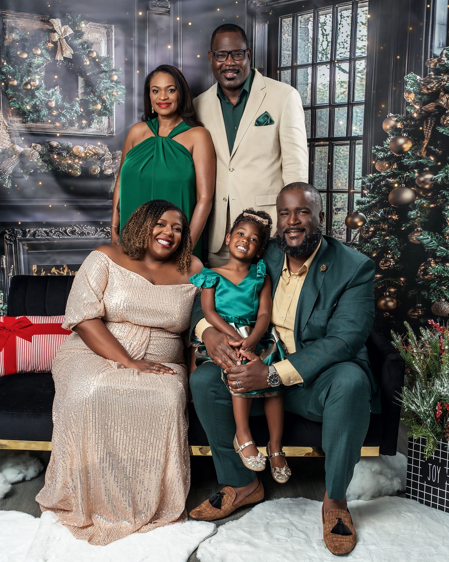 An elegantly dressed family of five poses for a holiday portrait in front of decorated Christmas trees.