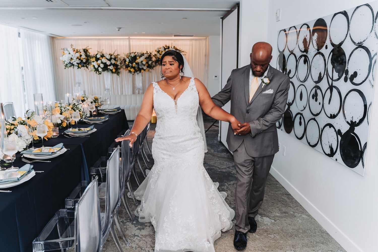 Couple walking through modern reception venue with elegant table settings and wall decor.