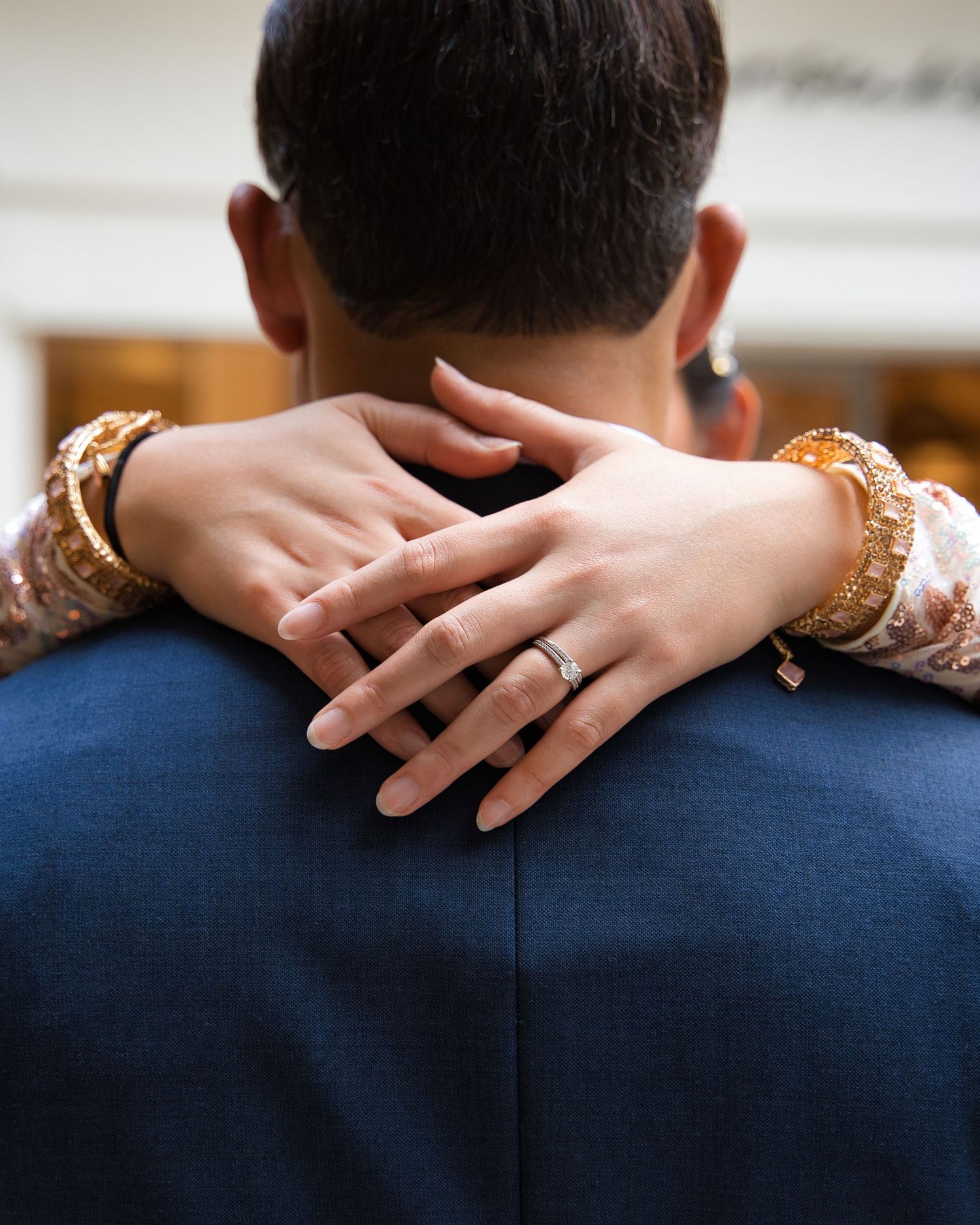 Close-up of hands with wedding ring embracing in lace sleeves against navy suit.