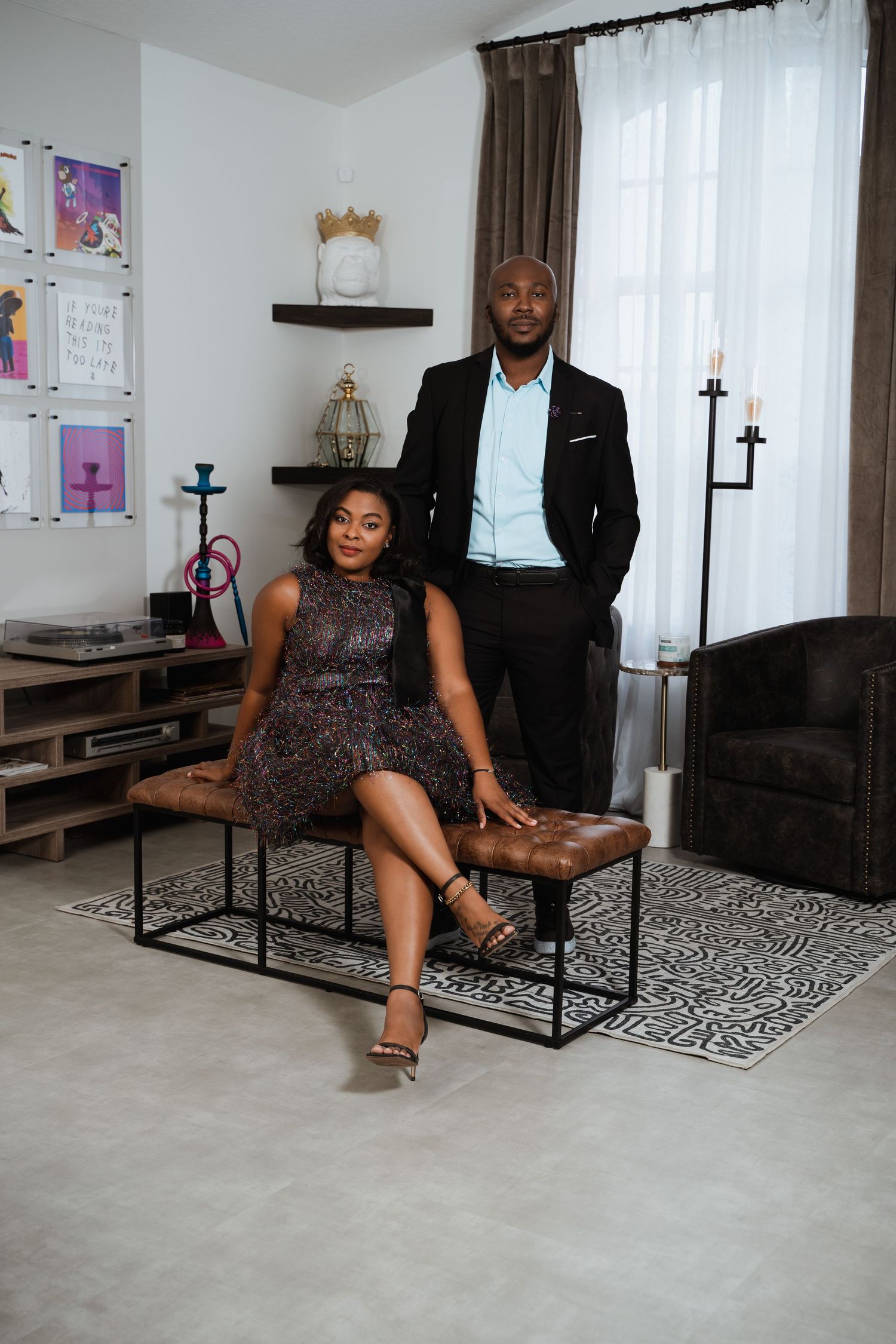 Stylish couple posing in elegant attire inside a modern decorated living space.