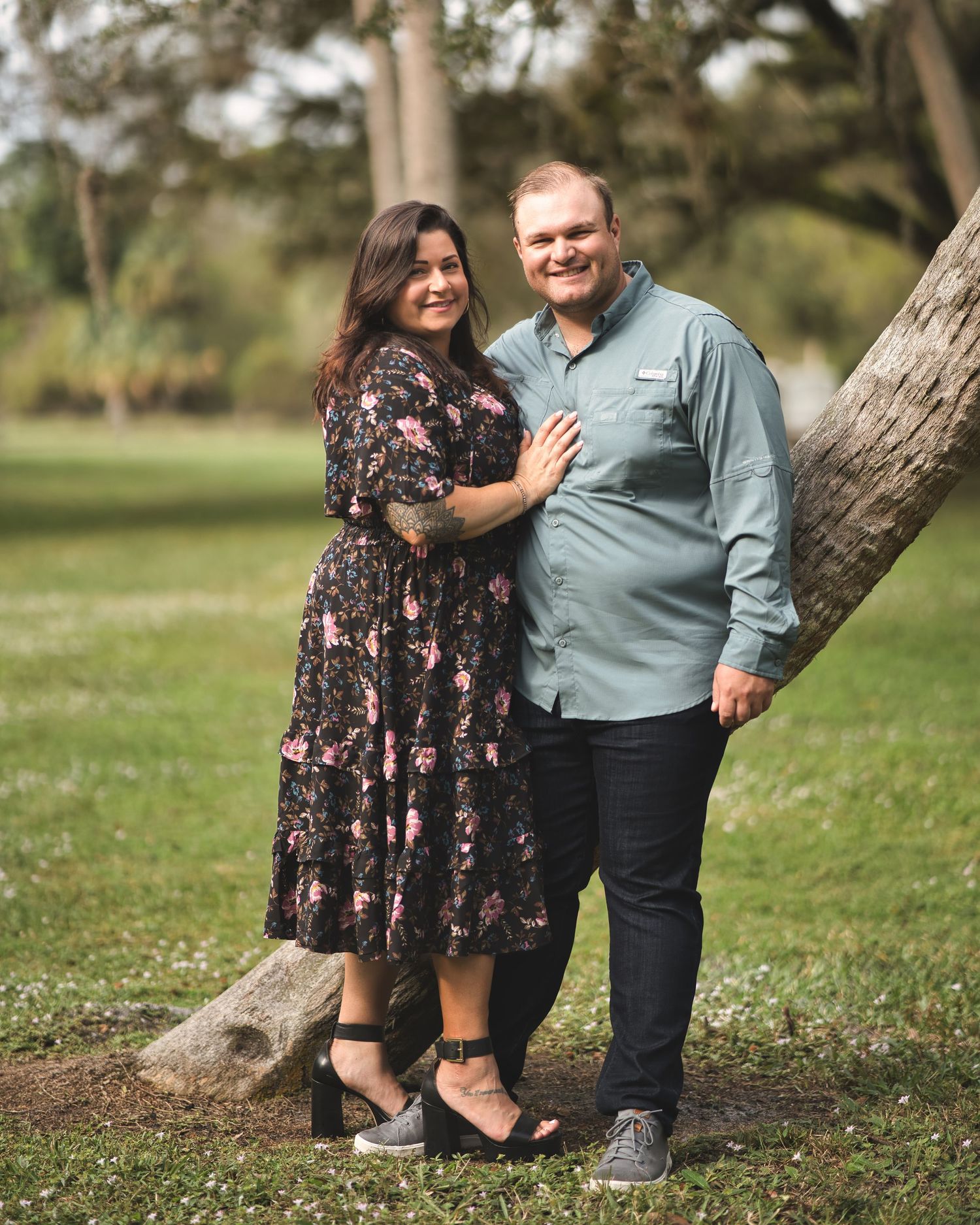 A romantic couple embracing against a tree in a park setting.