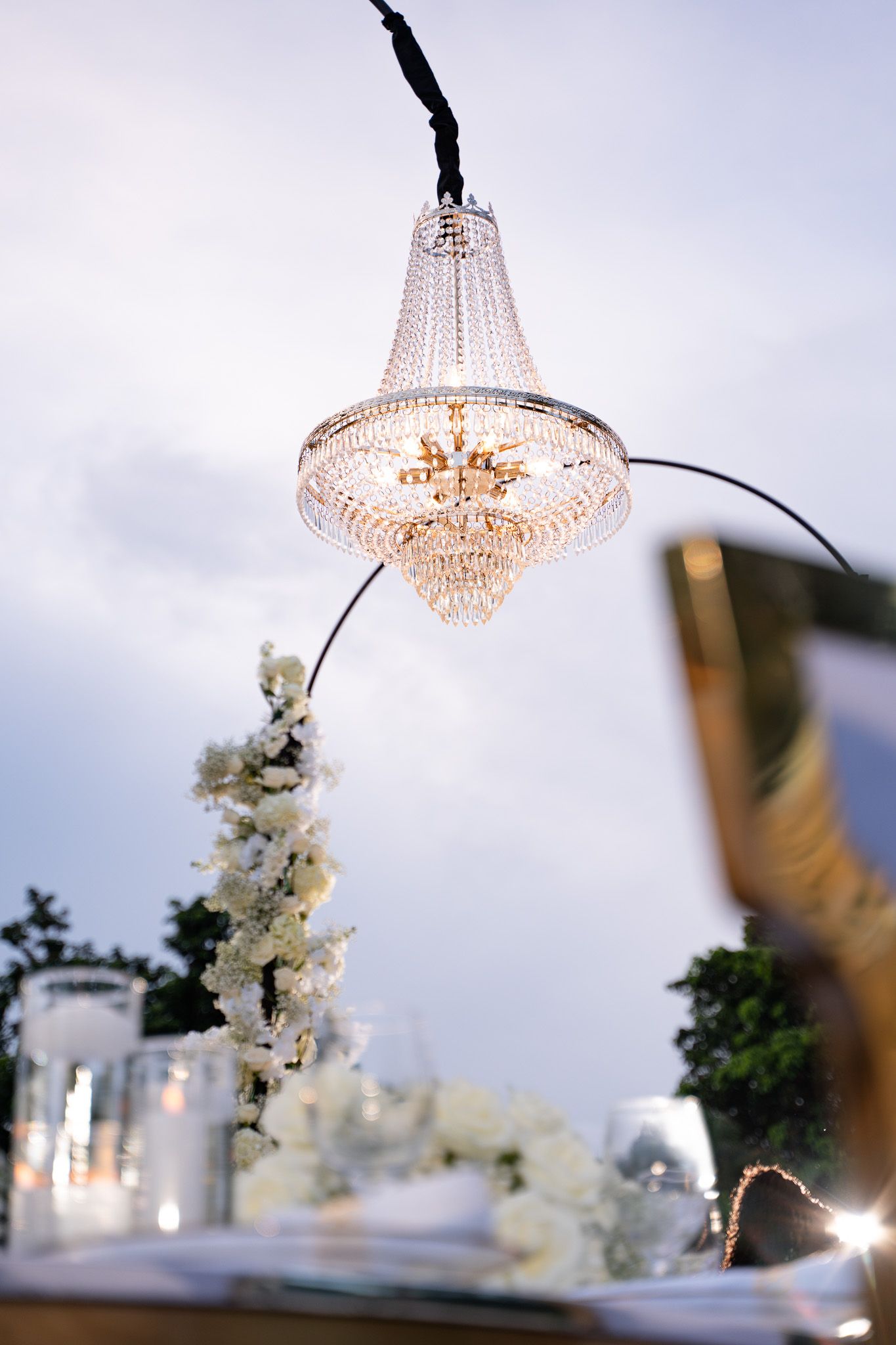 Elegant crystal chandelier hangs over white floral decorations at an upscale event setting.