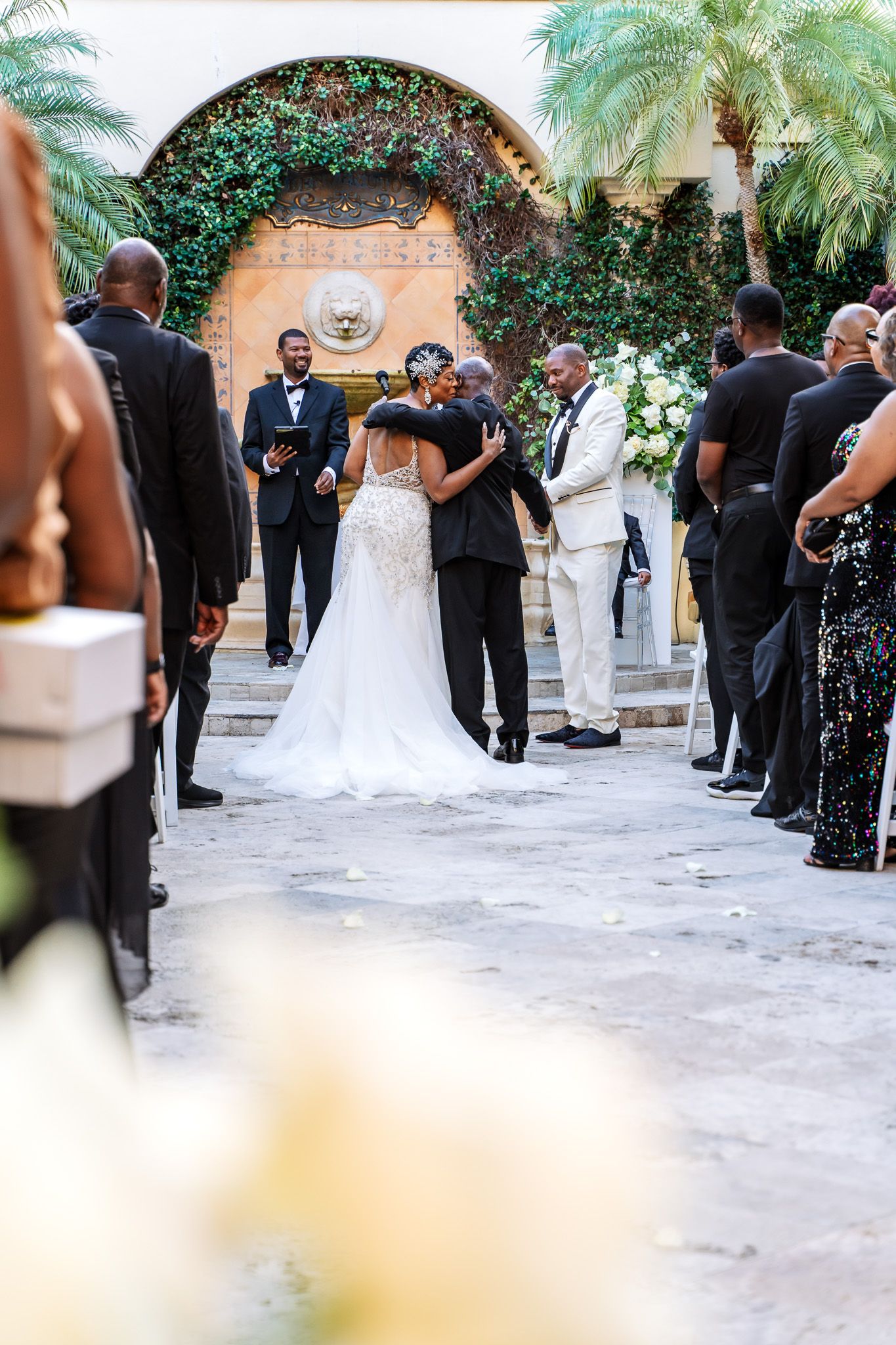 Wedding ceremony in a tropical courtyard with palm trees and decorative archway.