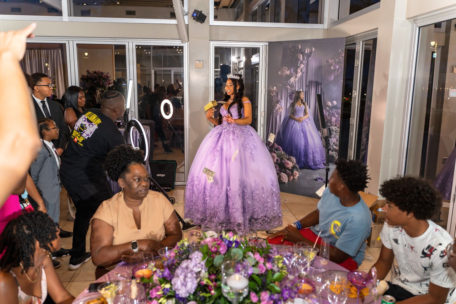 Guests gather around decorated tables at a formal celebration with purple decor and floral arrangements.