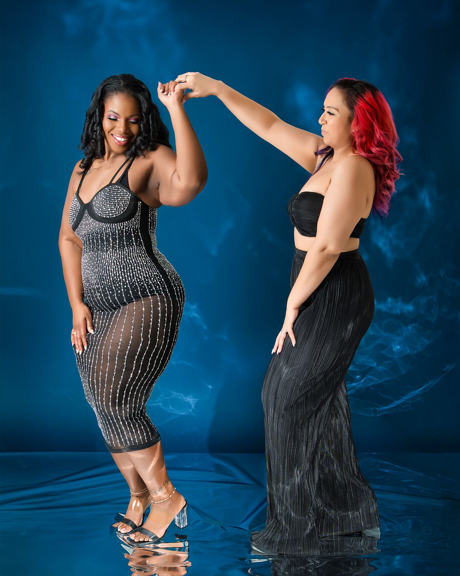 Two friends in evening wear dancing against dramatic blue background.