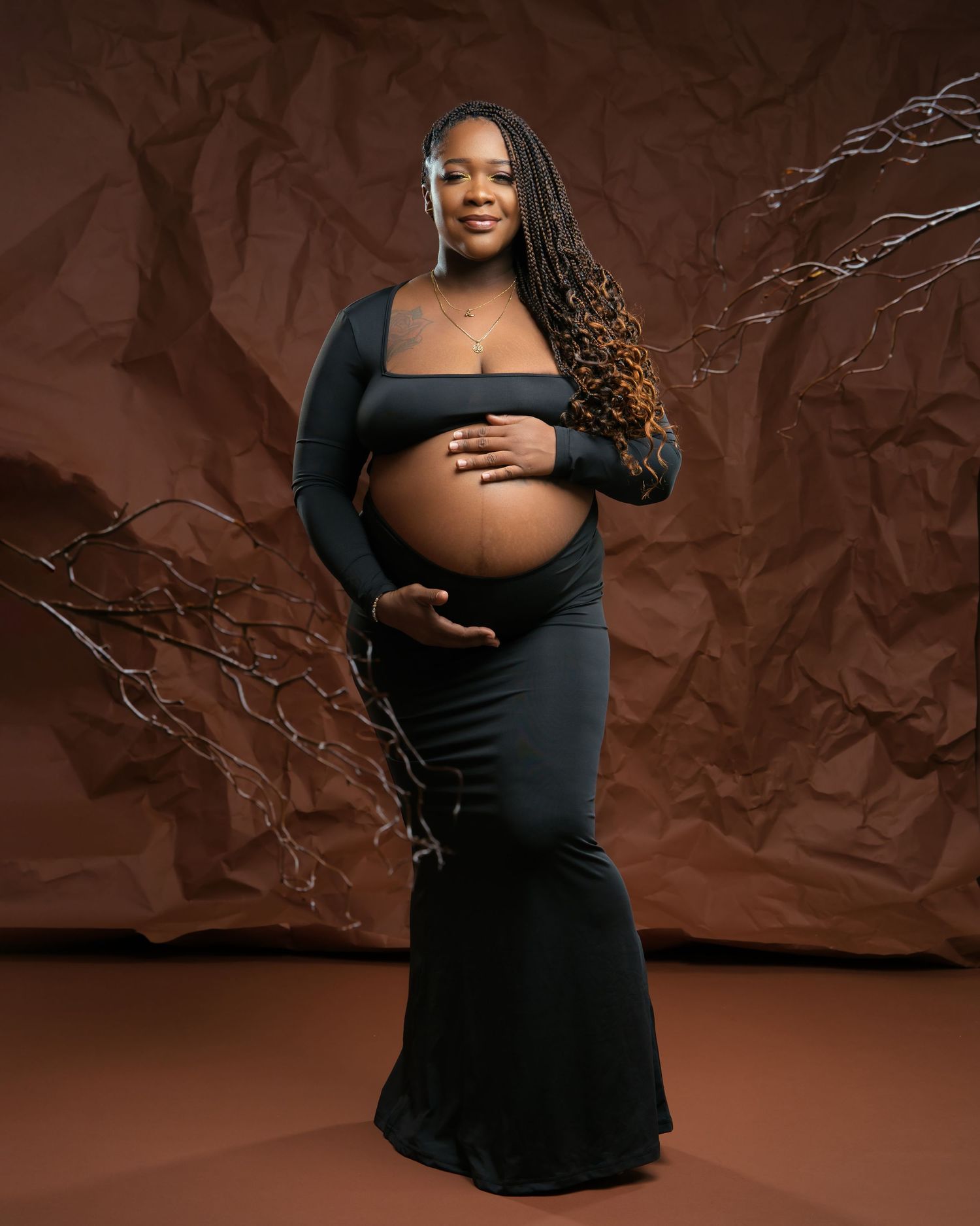 A dramatic maternity photo shows an expectant mother in a black dress against a brown backdrop.