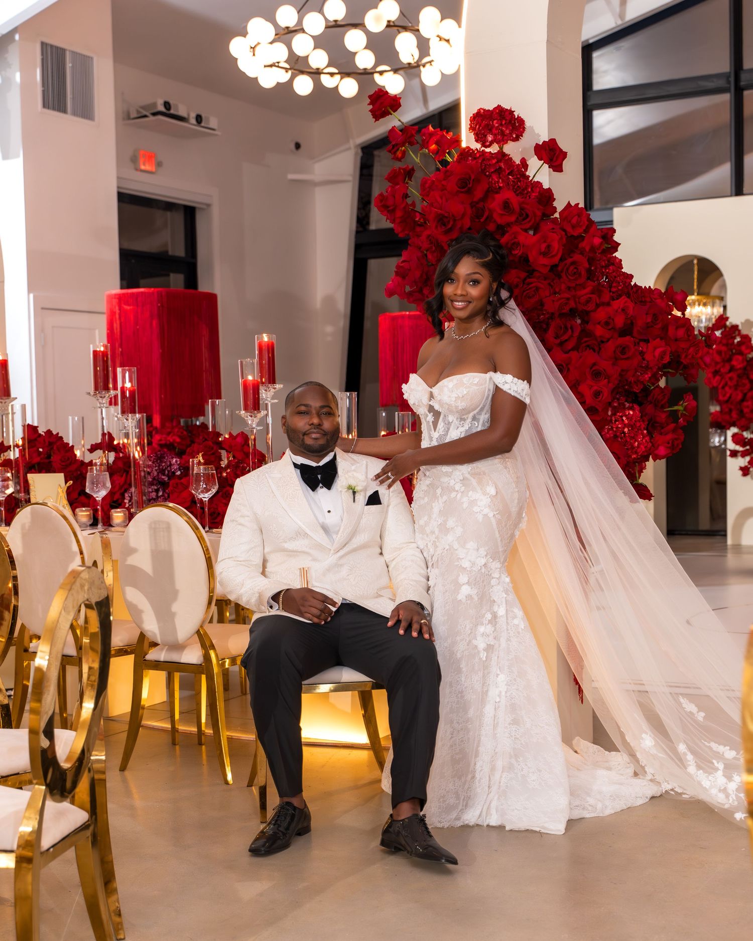 A wedding party in white and black attire poses in front of red floral decorations.