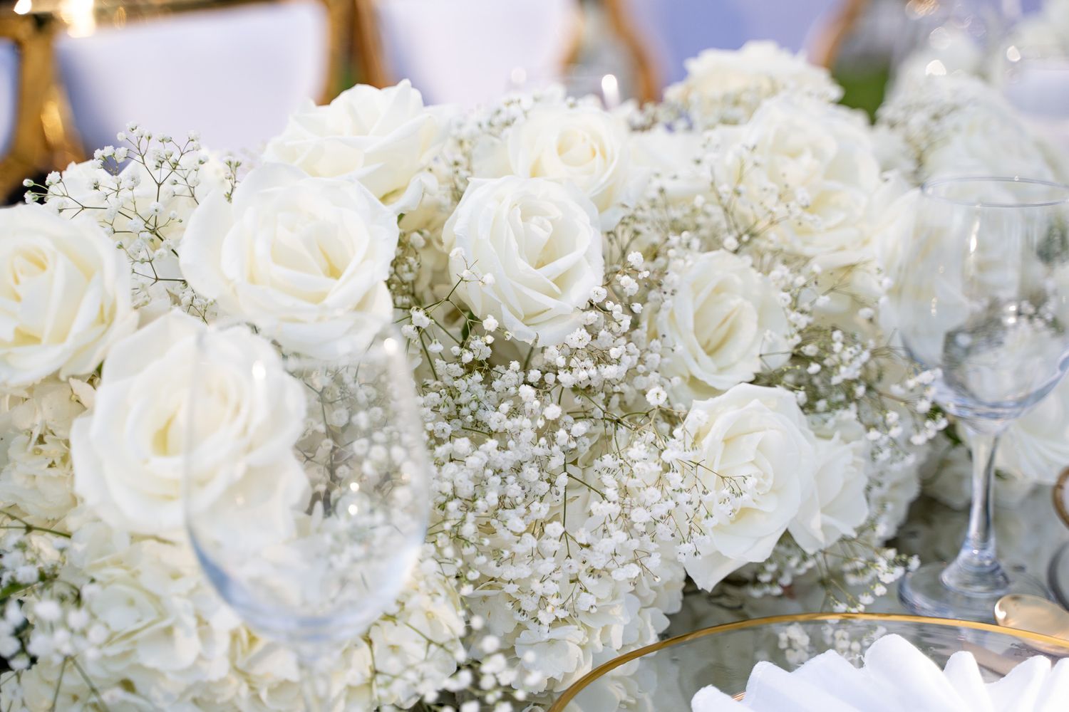 White roses and baby's breath flowers create an elegant wedding reception table arrangement against a light background.