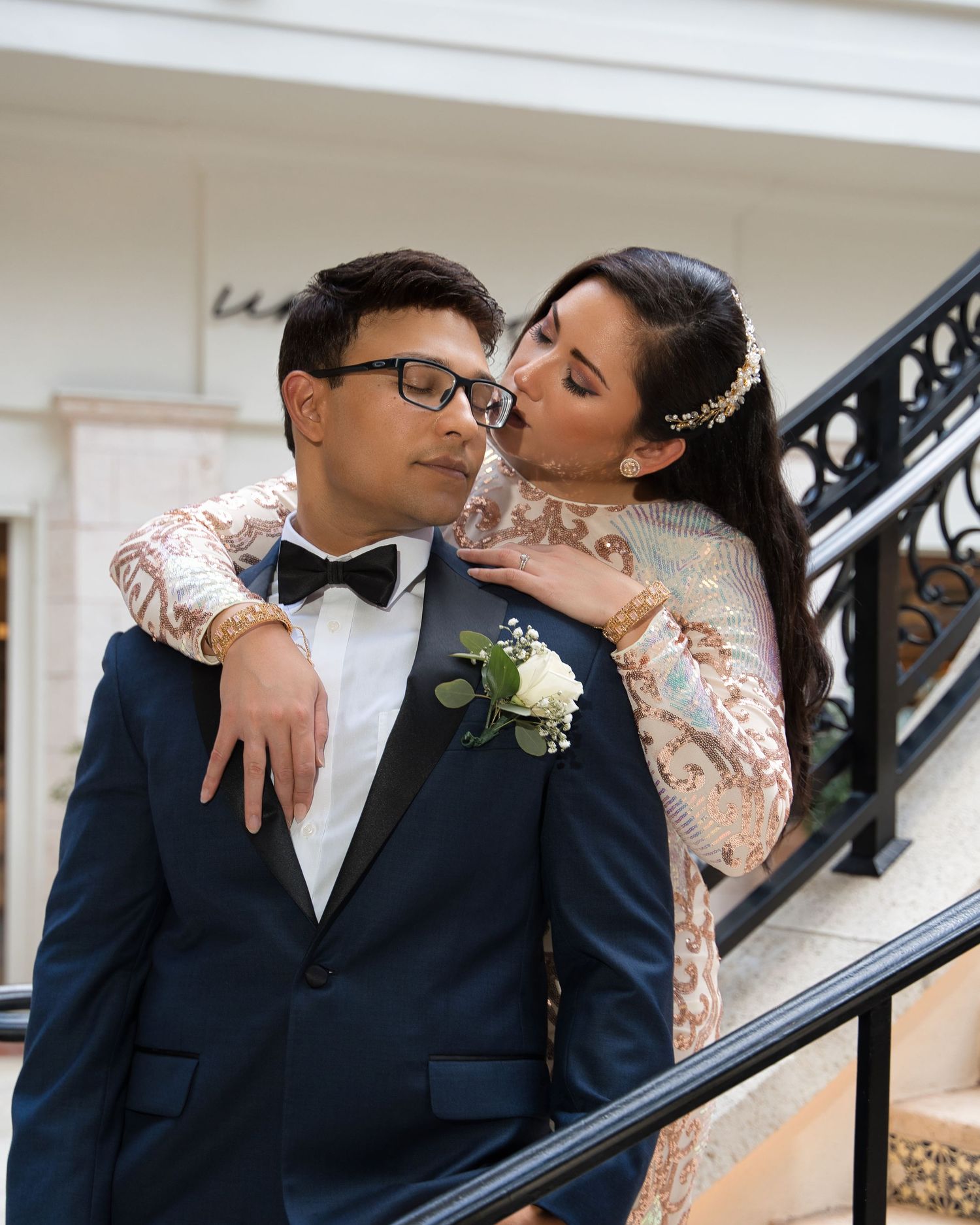 Romantic couple embrace on an elegant staircase in formal wedding attire.