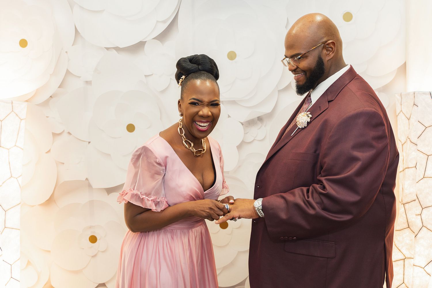 A couple shares a joyful moment during their wedding ceremony against a white backdrop with gold accents.