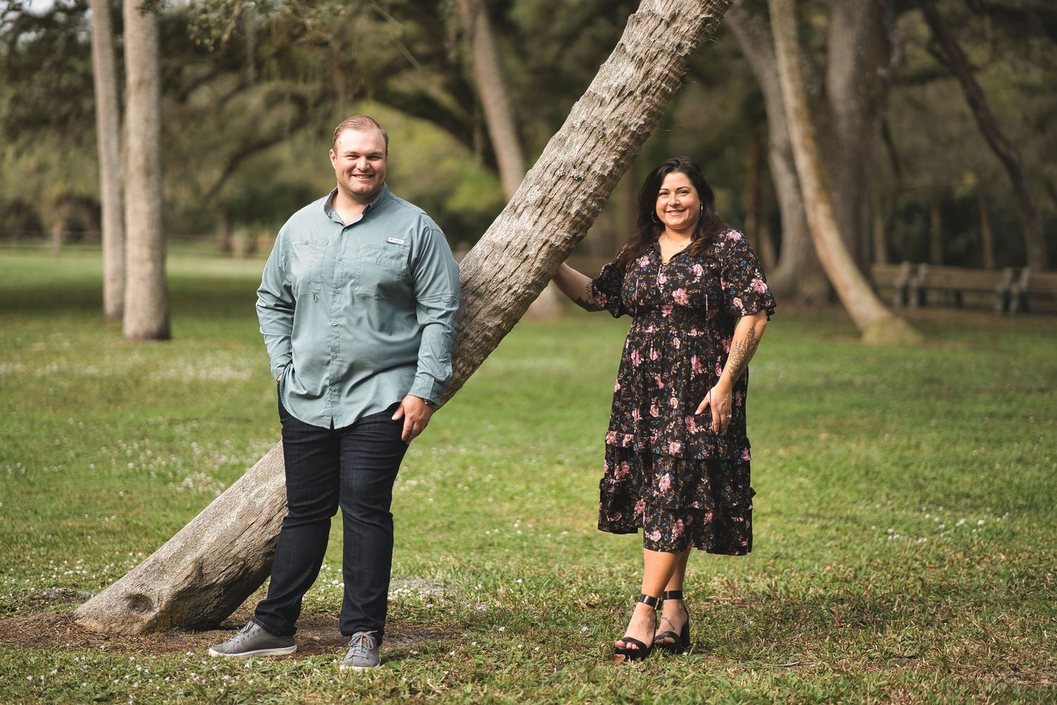 Couple poses near a leaning tree trunk in a scenic park.