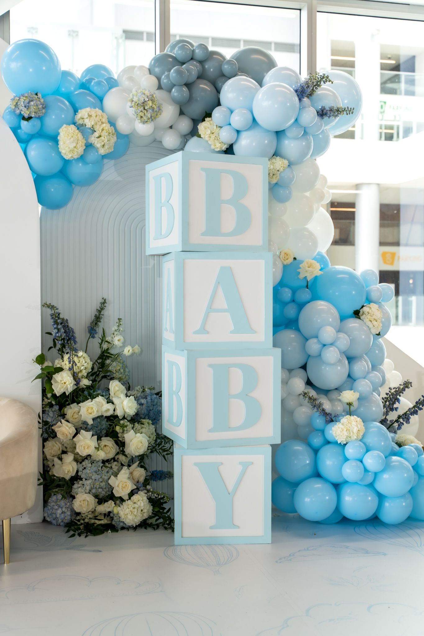 Baby shower decoration featuring stacked BABY blocks with blue and white balloon garland.