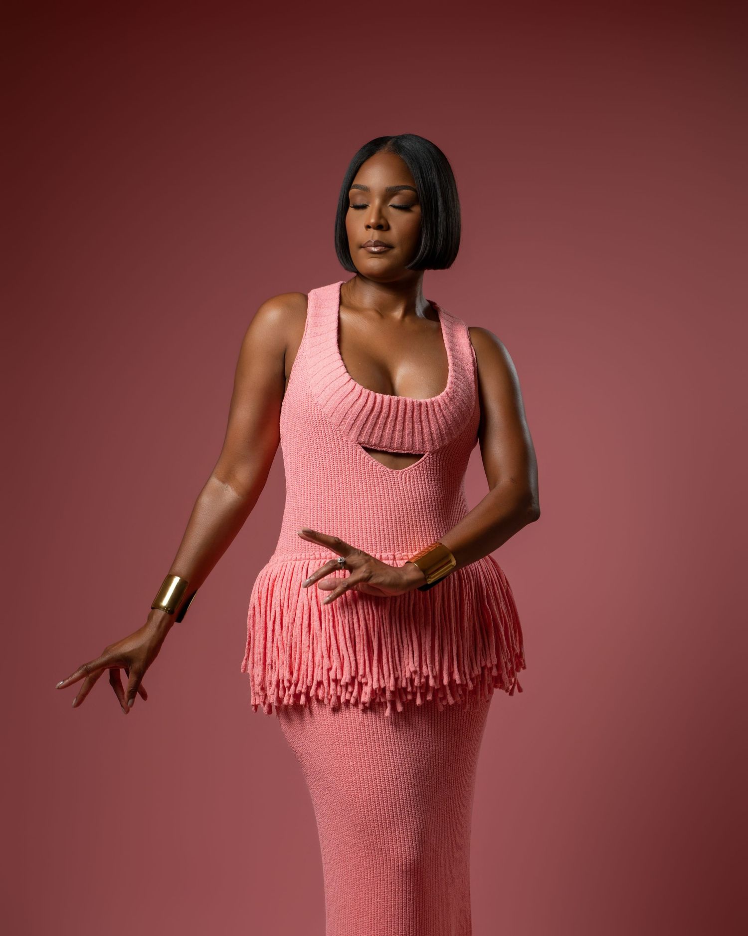 A model in a pink knit dress with fringe detail poses against a burgundy backdrop in a fashion photoshoot sequence.