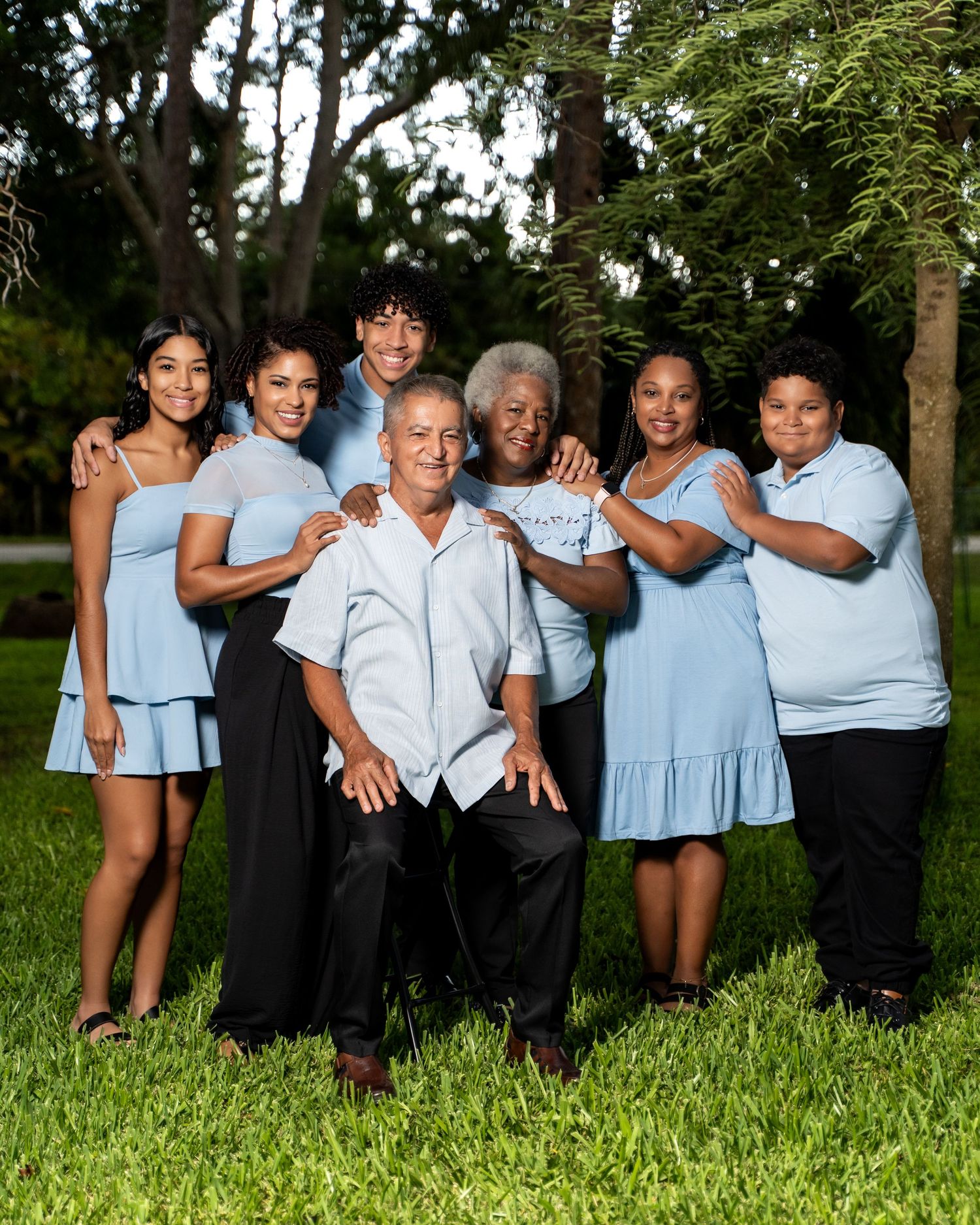 Family group in coordinated light blue and black outfits posing together on grass during outdoor photo session.