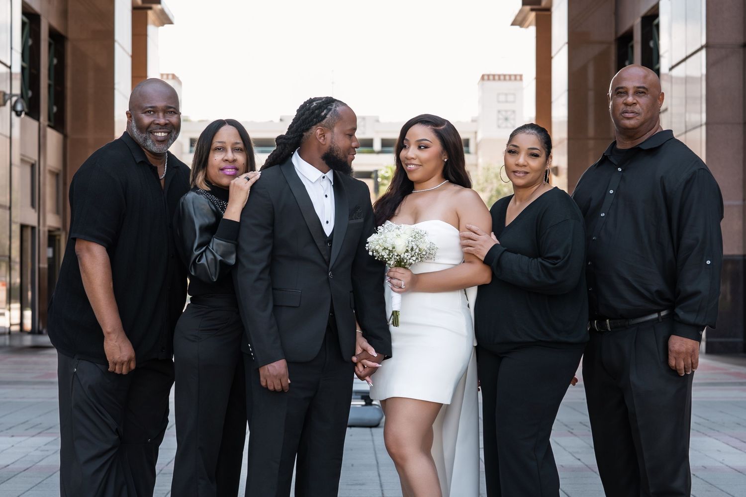 A group of well-dressed people in formal black and white attire pose together for a photo outdoors.