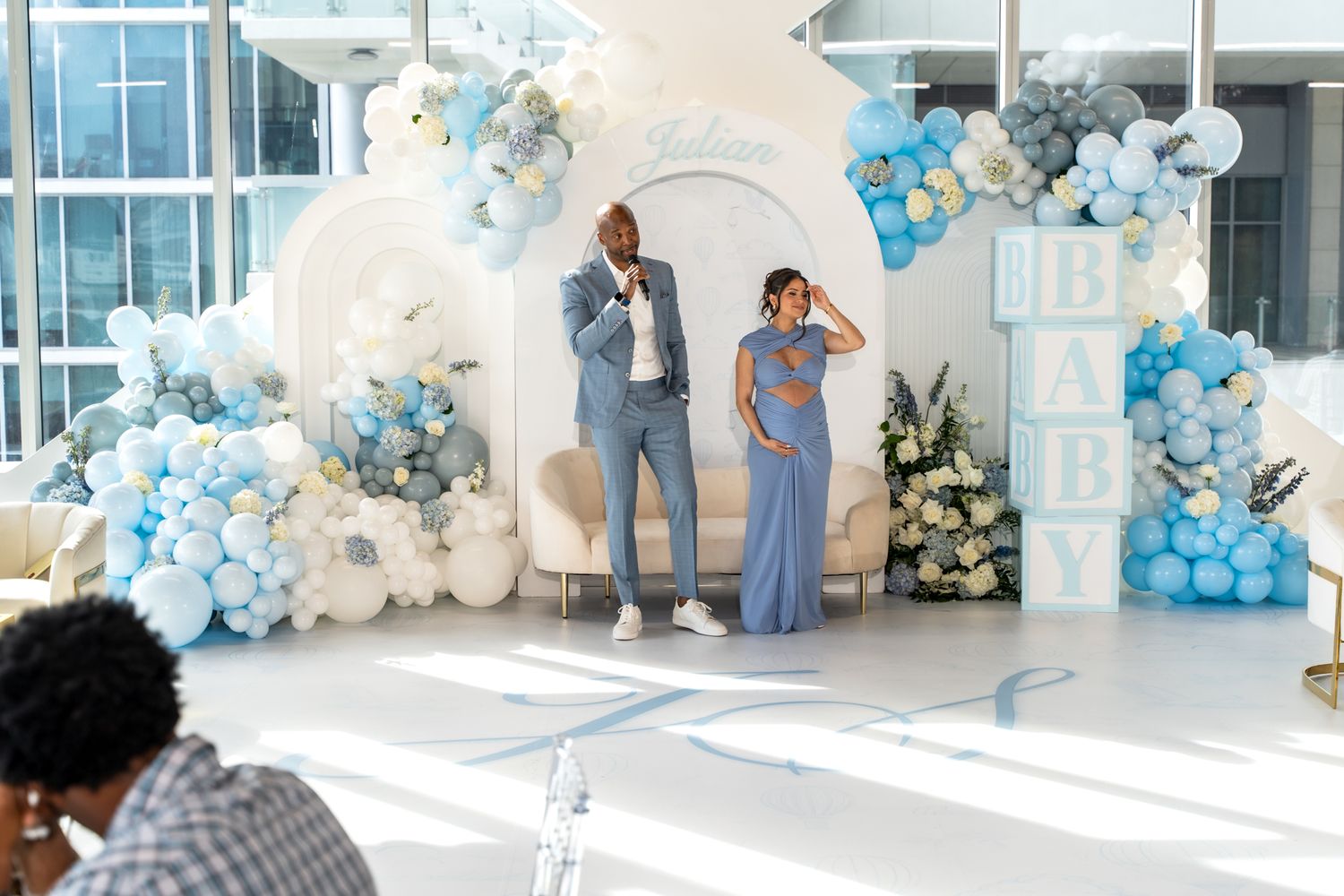 Candid moment during baby shower with couple posing against decorative blue and white balloon arch.