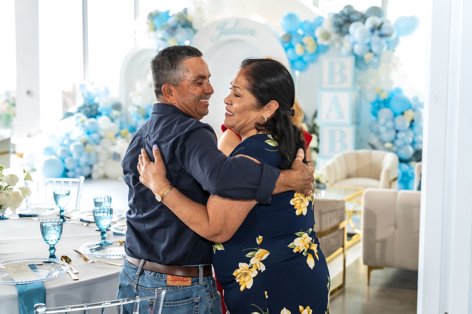 Loving couple embracing at baby shower celebration with blue floral decorations in background.