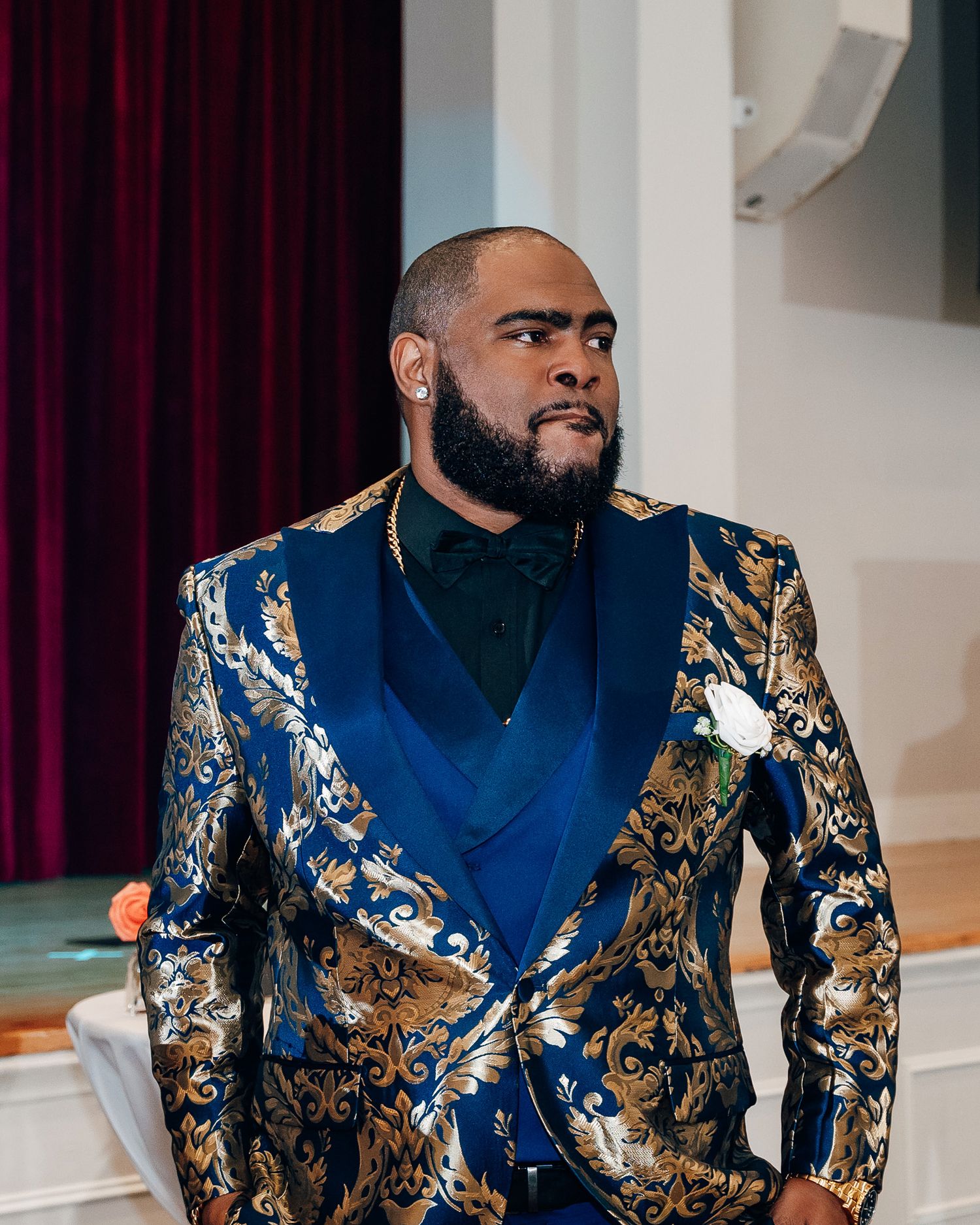 Groom wearing an elegant blue and gold brocade tuxedo jacket at wedding ceremony.