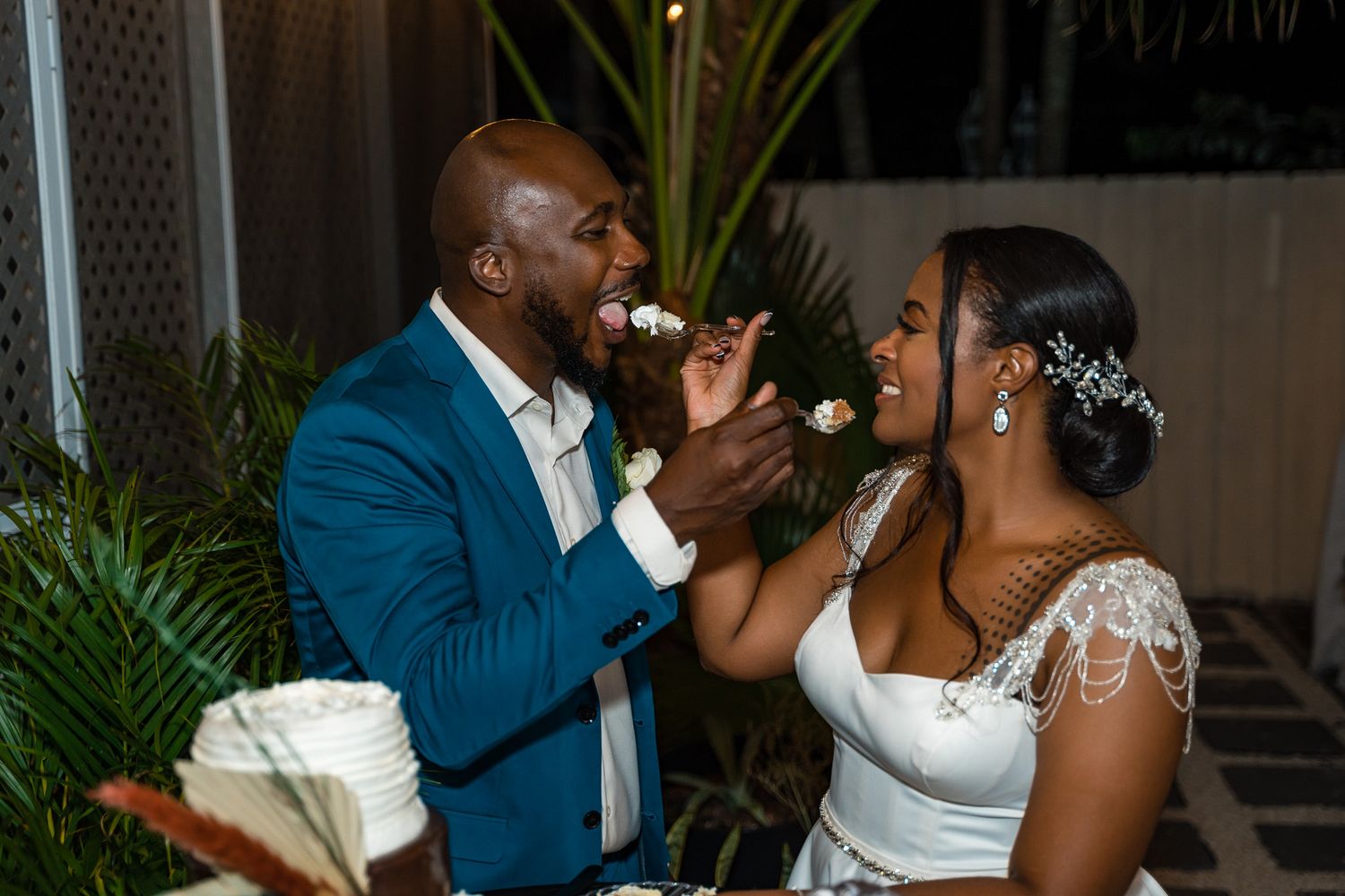 Wedding couple joyfully sharing a bite of wedding cake during their reception celebration.